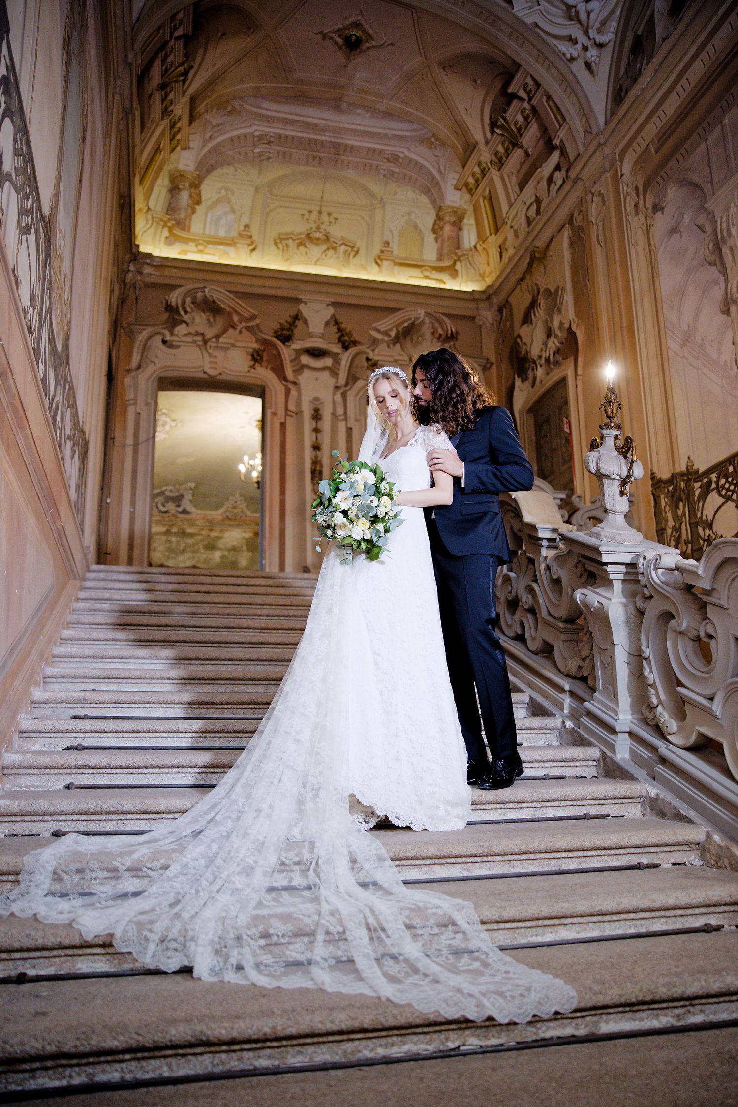 A romantic wedding scene on an ornate marble staircase in a luxurious palace with baroque architectural details.