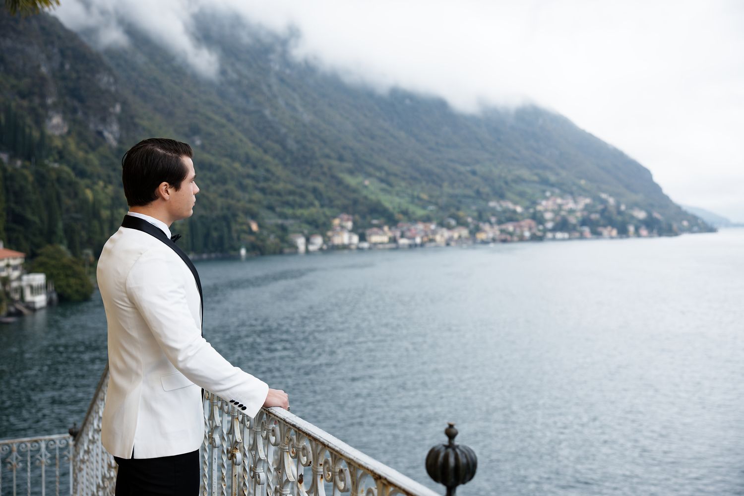 Person in white jacket overlooking scenic coastal town and mountains.