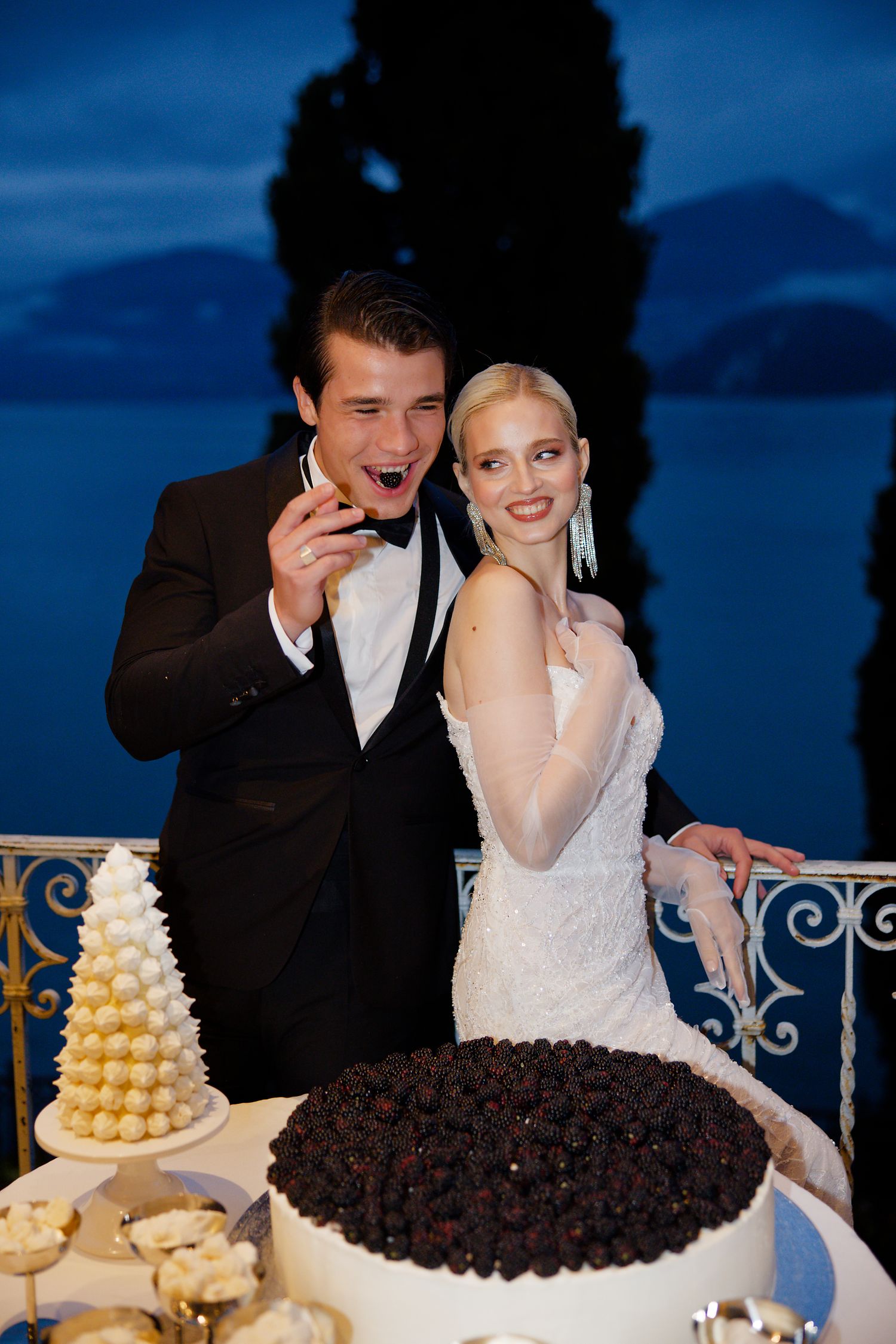A joyful cake-cutting moment at an evening wedding reception with two cakes on display.