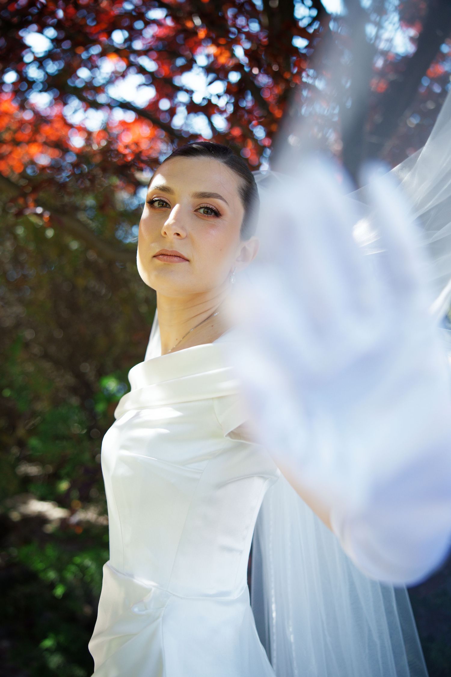 Artistic bridal portrait with flowing white fabric against autumn foliage background.