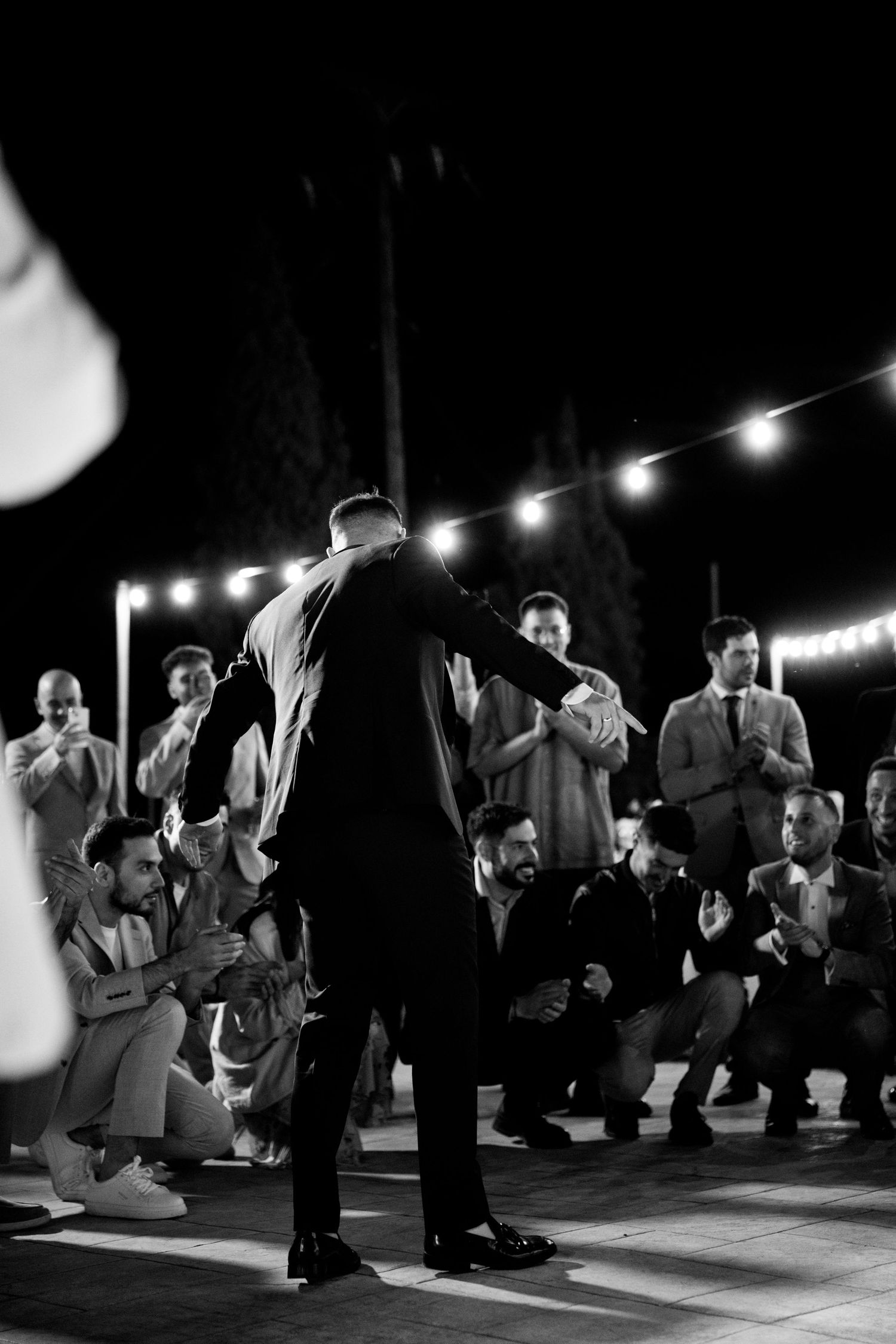 Black and white photo of dancers performing under string lights at outdoor venue.