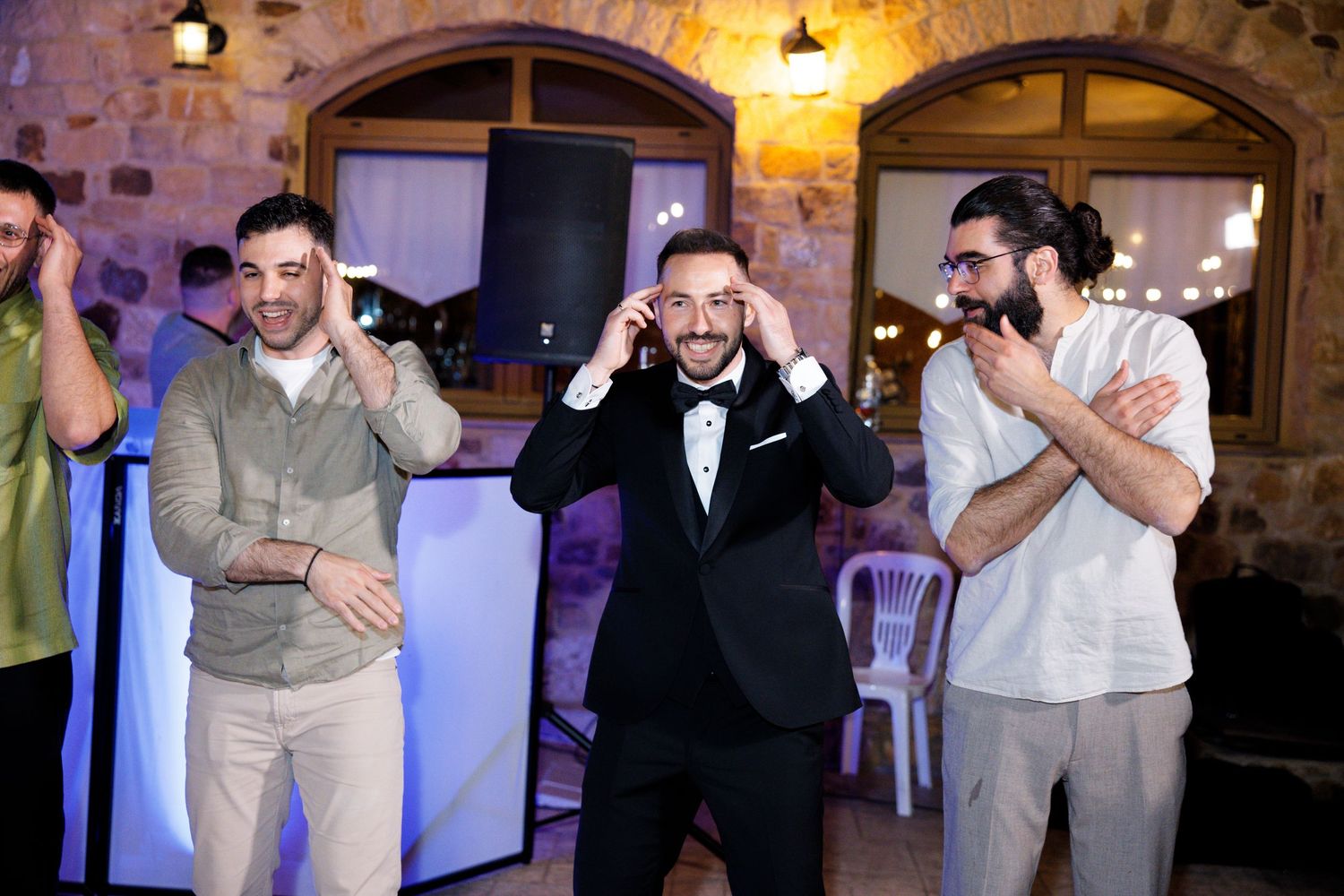 Wedding party members dancing and celebrating with joyful expressions at an indoor venue.
