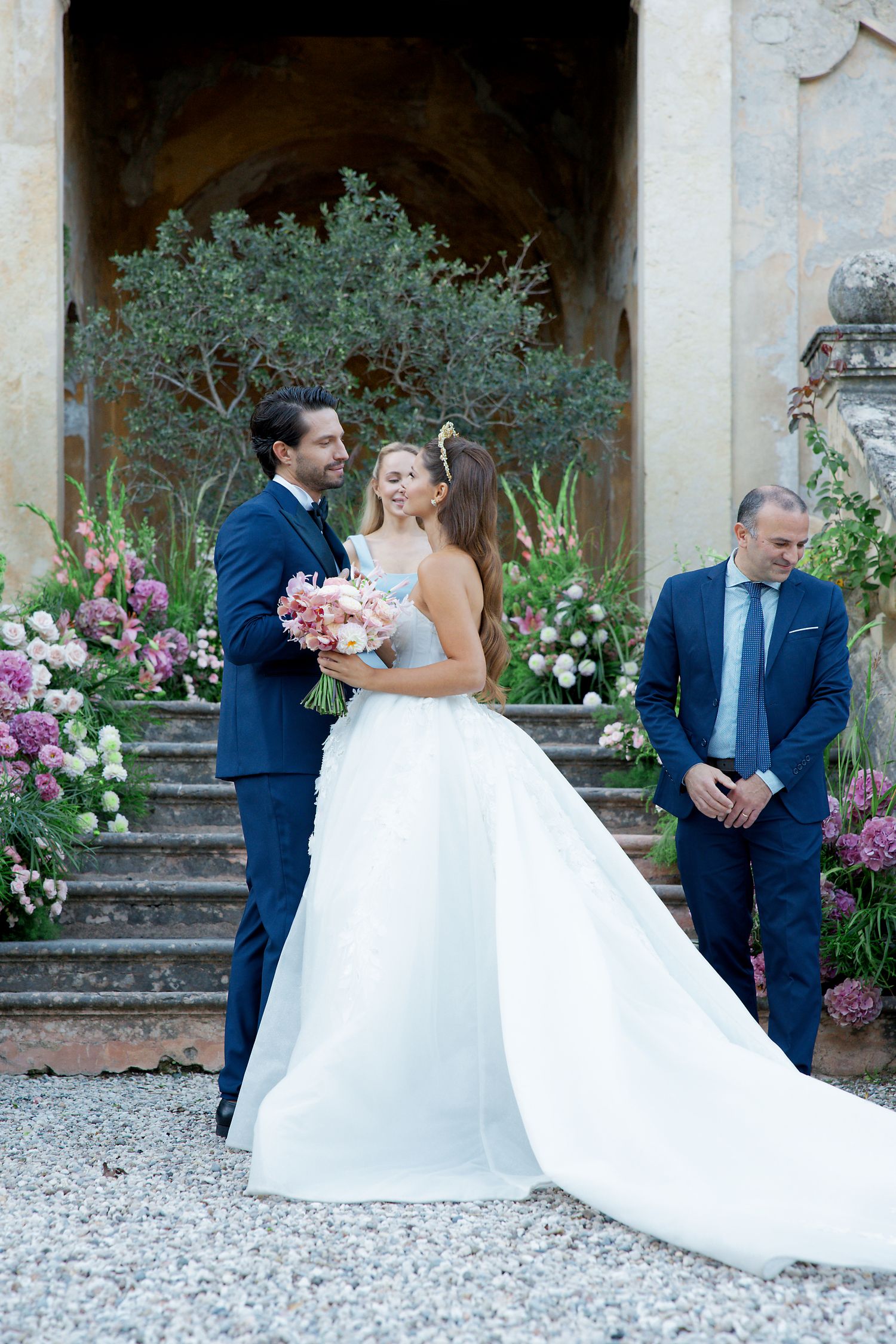 Elegant wedding moment captured on stone steps decorated with pink and white flowers and greenery.
