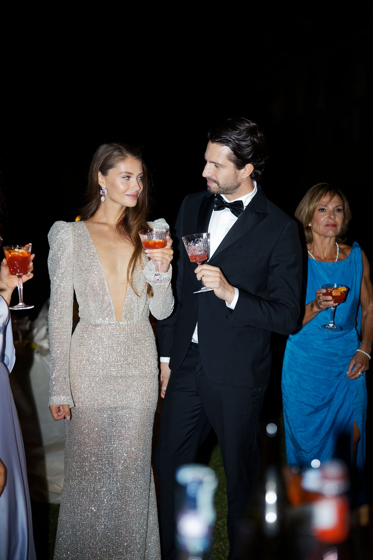 Elegant wedding reception with guests in formal attire holding cocktails at night.