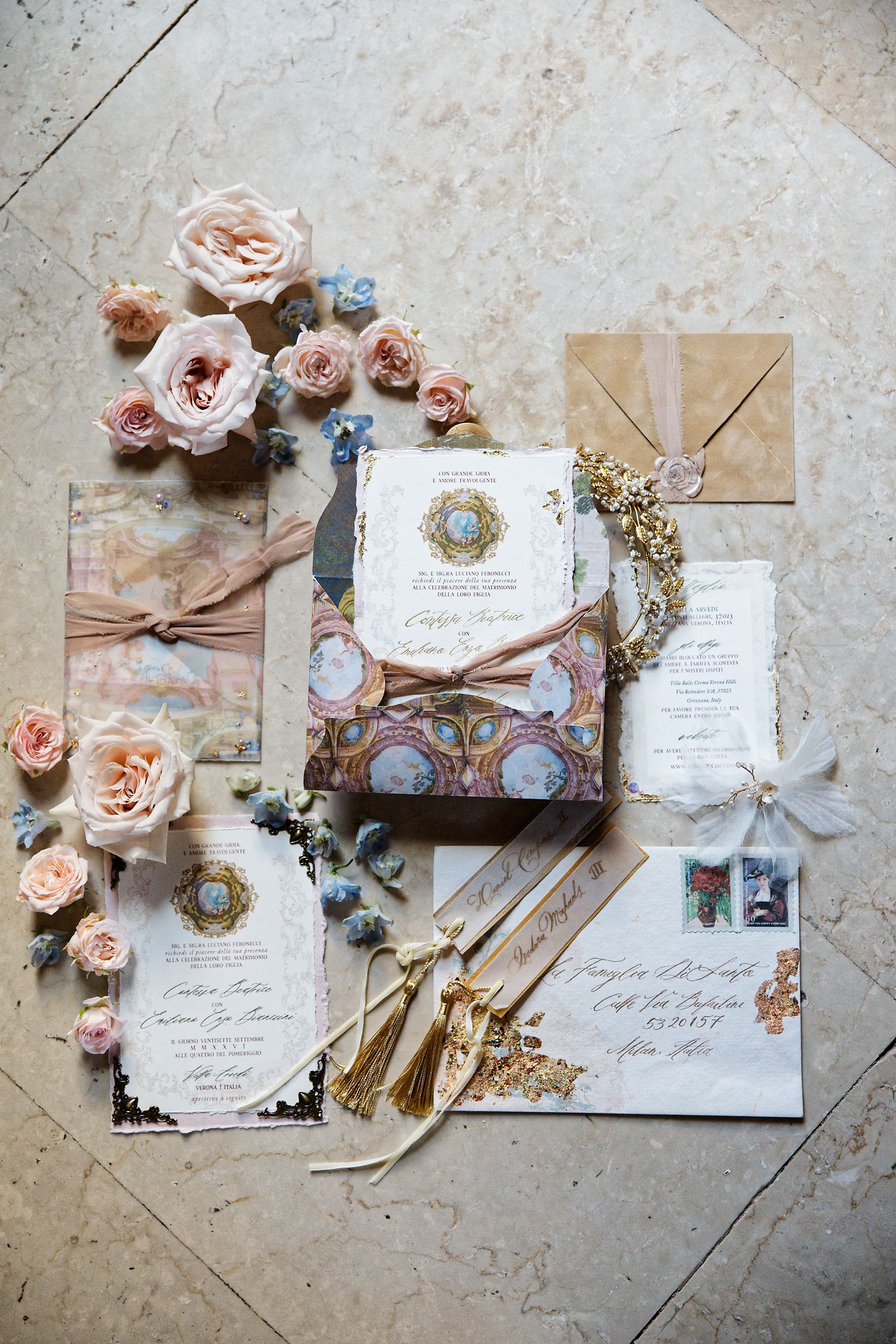 Elegant wedding stationery suite with blush roses, tassels and vintage-inspired designs on a light stone surface.