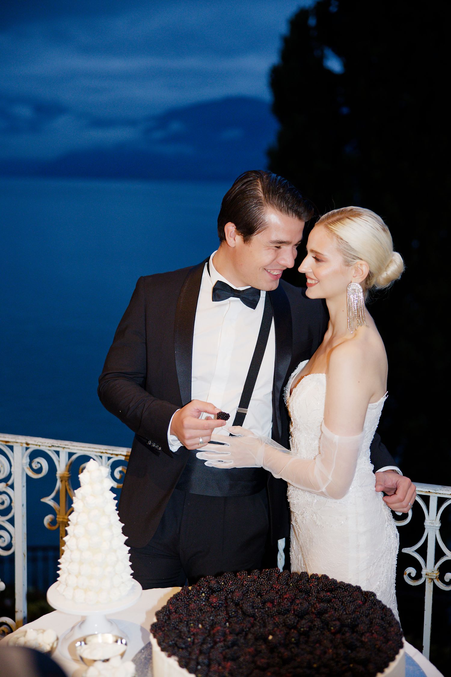 Romantic nighttime wedding portrait by ornate railing with cakes.