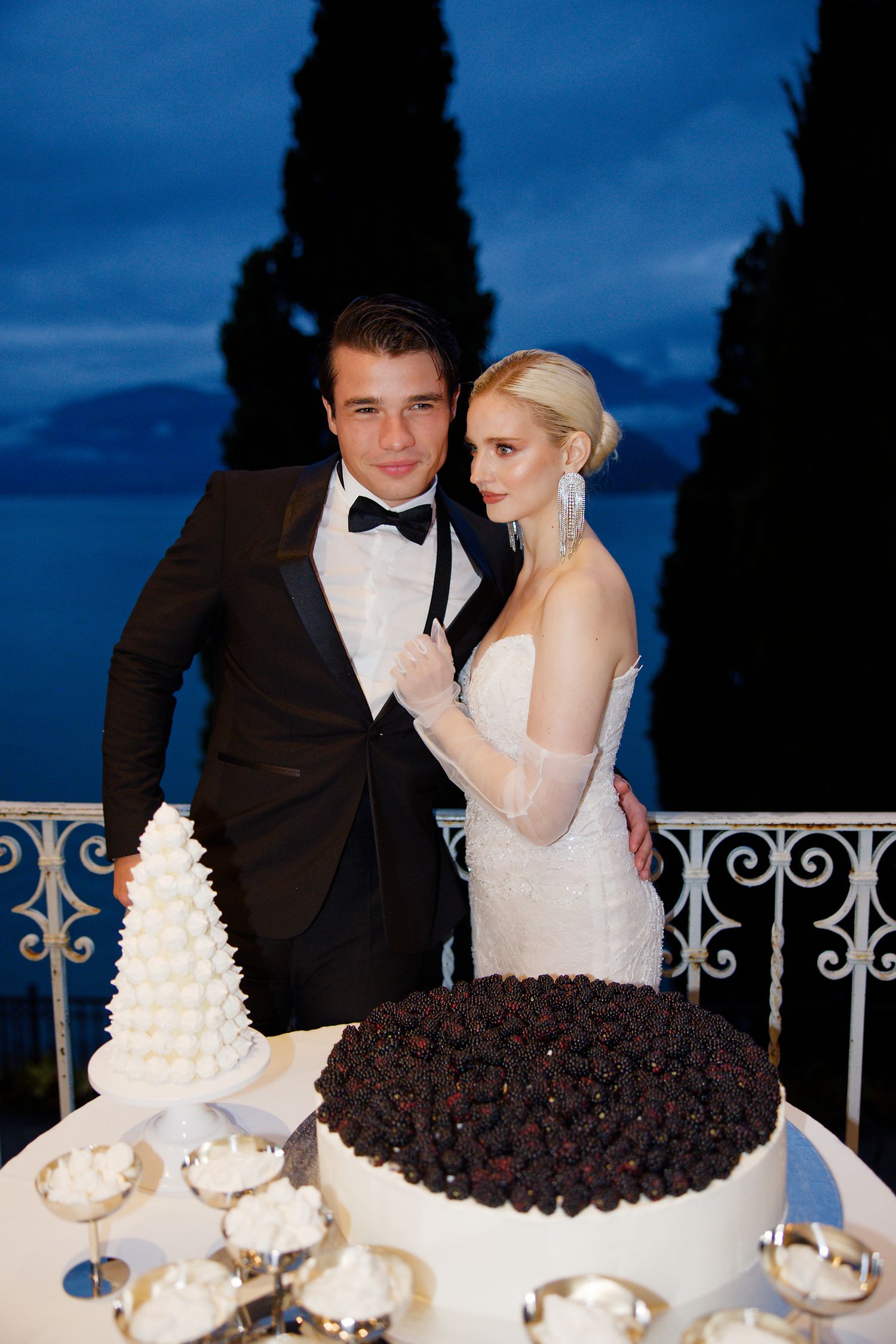 Evening wedding cake cutting scene with formal attire and romantic blue twilight backdrop.