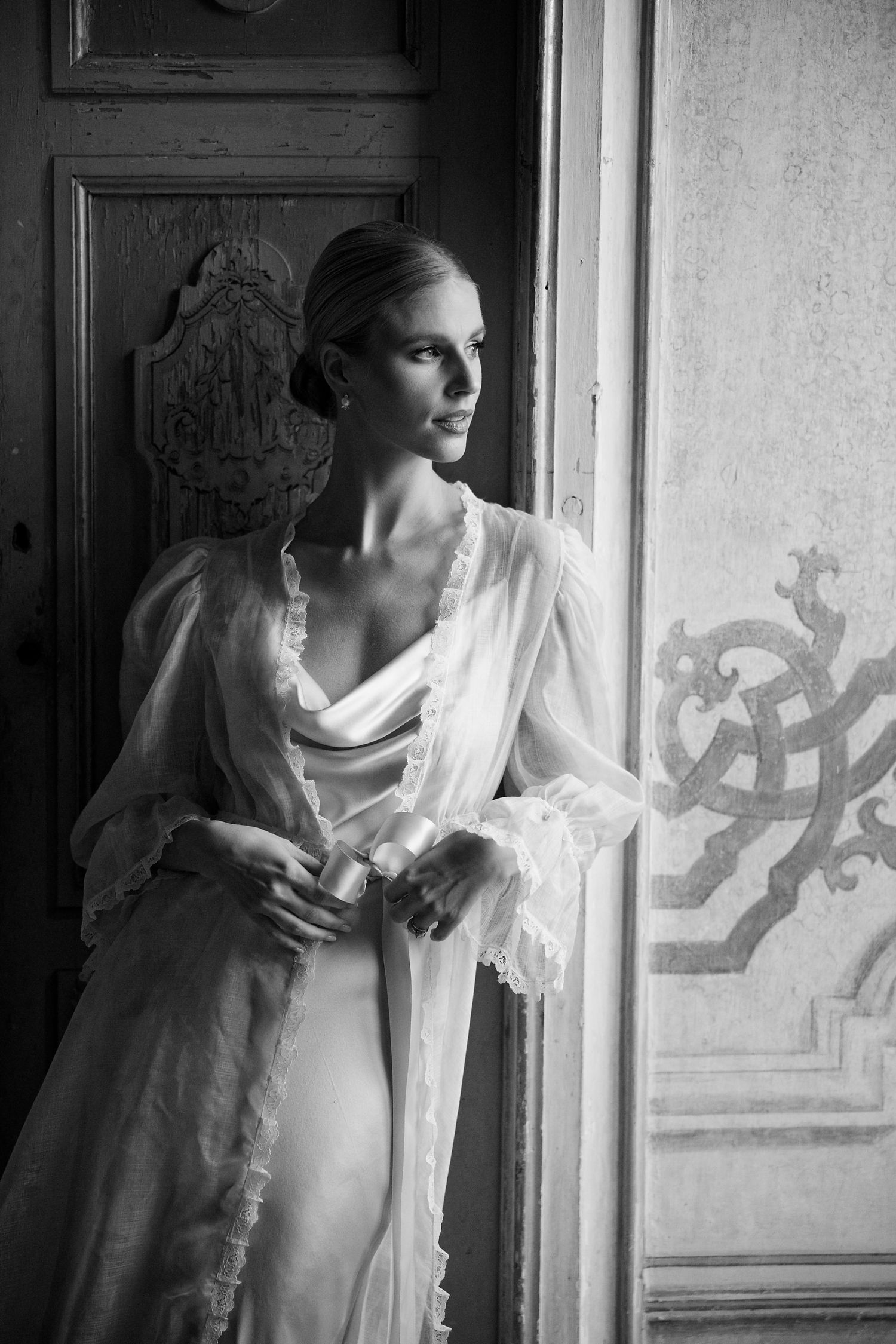 Classic black and white portrait near an ornate window with vintage architectural details.