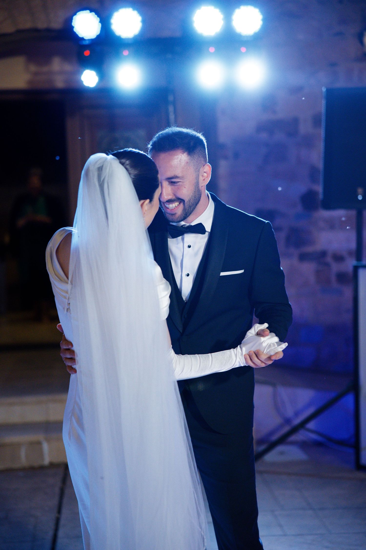 A romantic first dance at a wedding reception with blue stage lighting in the background.
