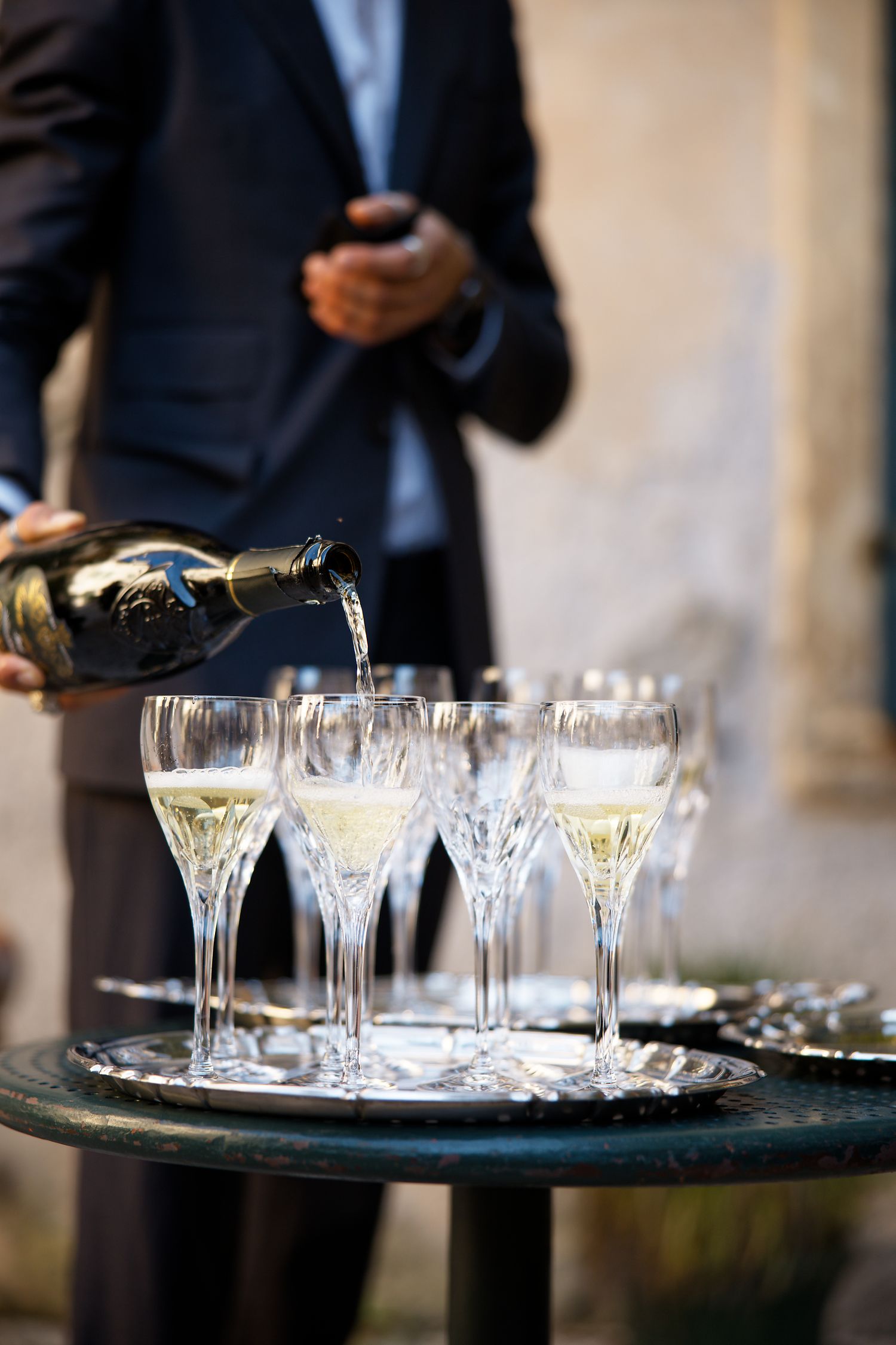 Champagne being poured into elegant crystal glasses on a round serving tray at an upscale event.