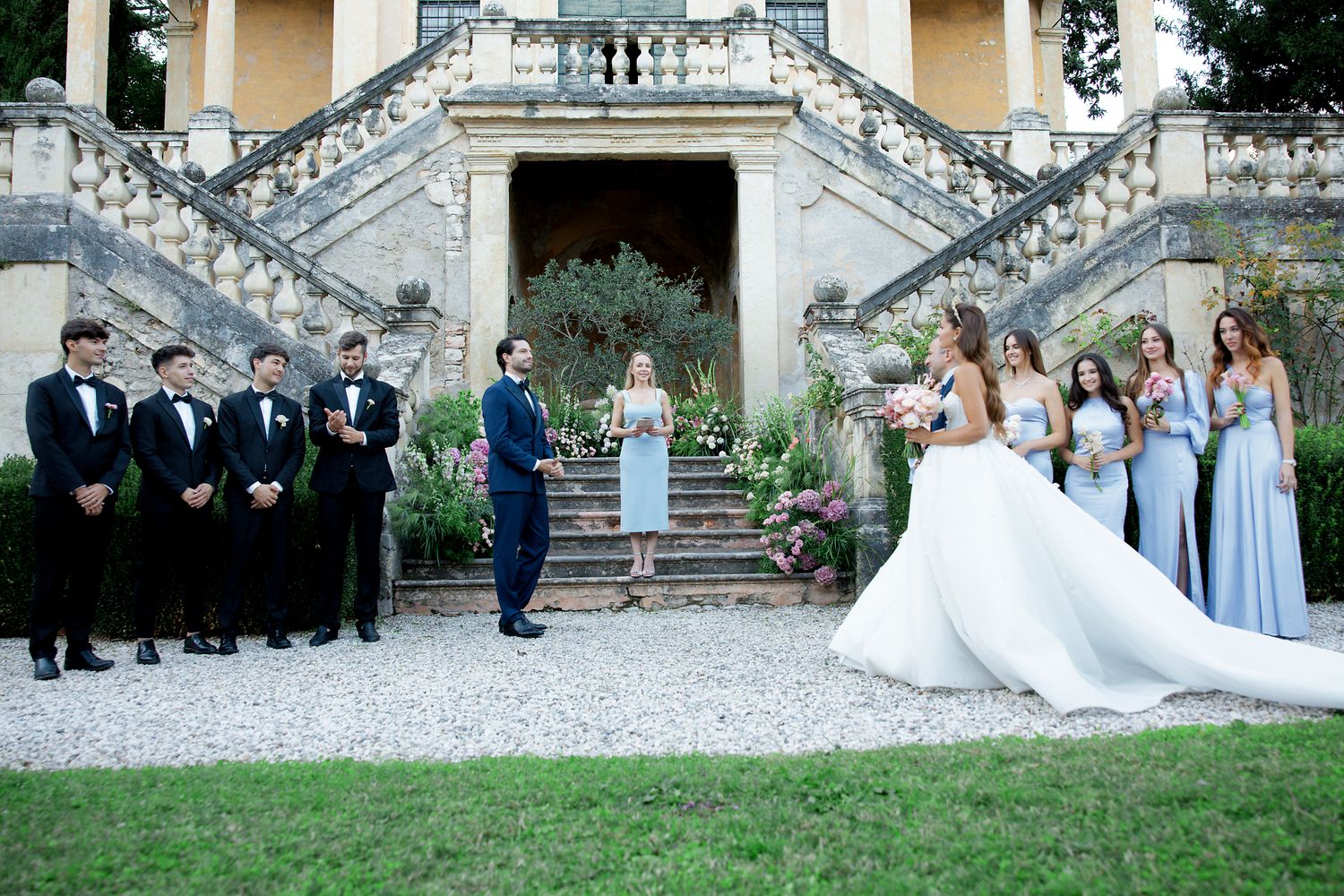 Wedding party arranged on grand stone staircase with bridal couple centered in elegant pose.