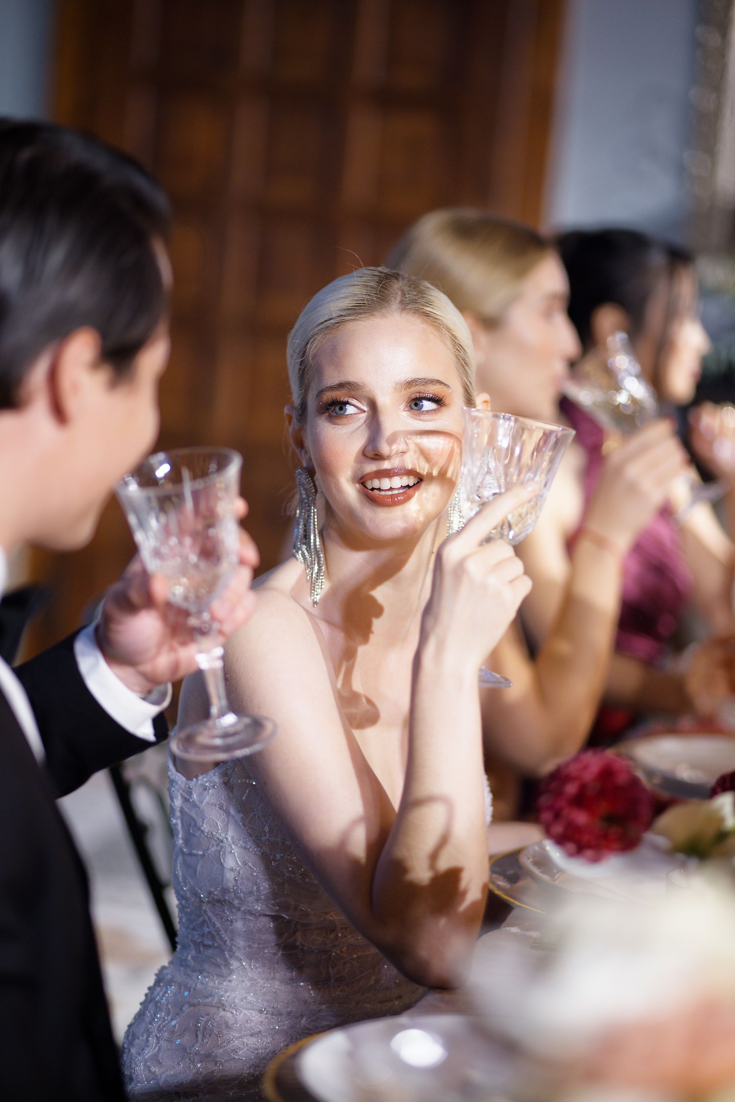Elegantly dressed guests share laughter and conversation over crystal glasses at a formal dinner party.