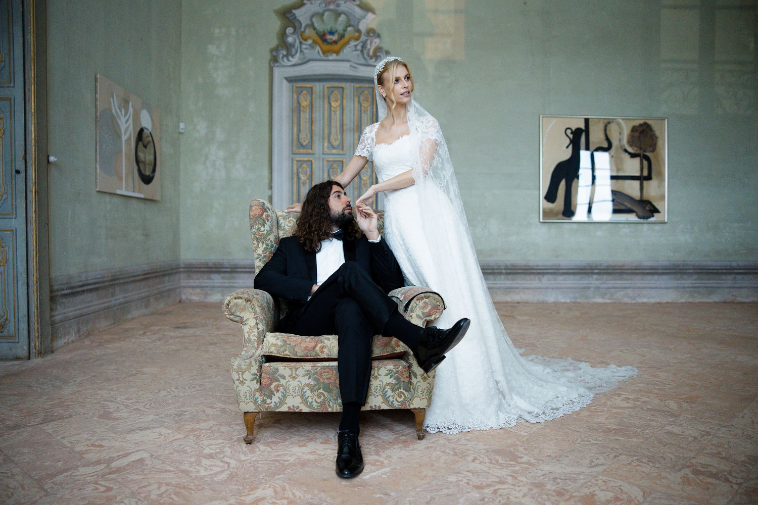Elegant wedding couple poses in ornate vintage room with antique furniture and decorative mirrors.