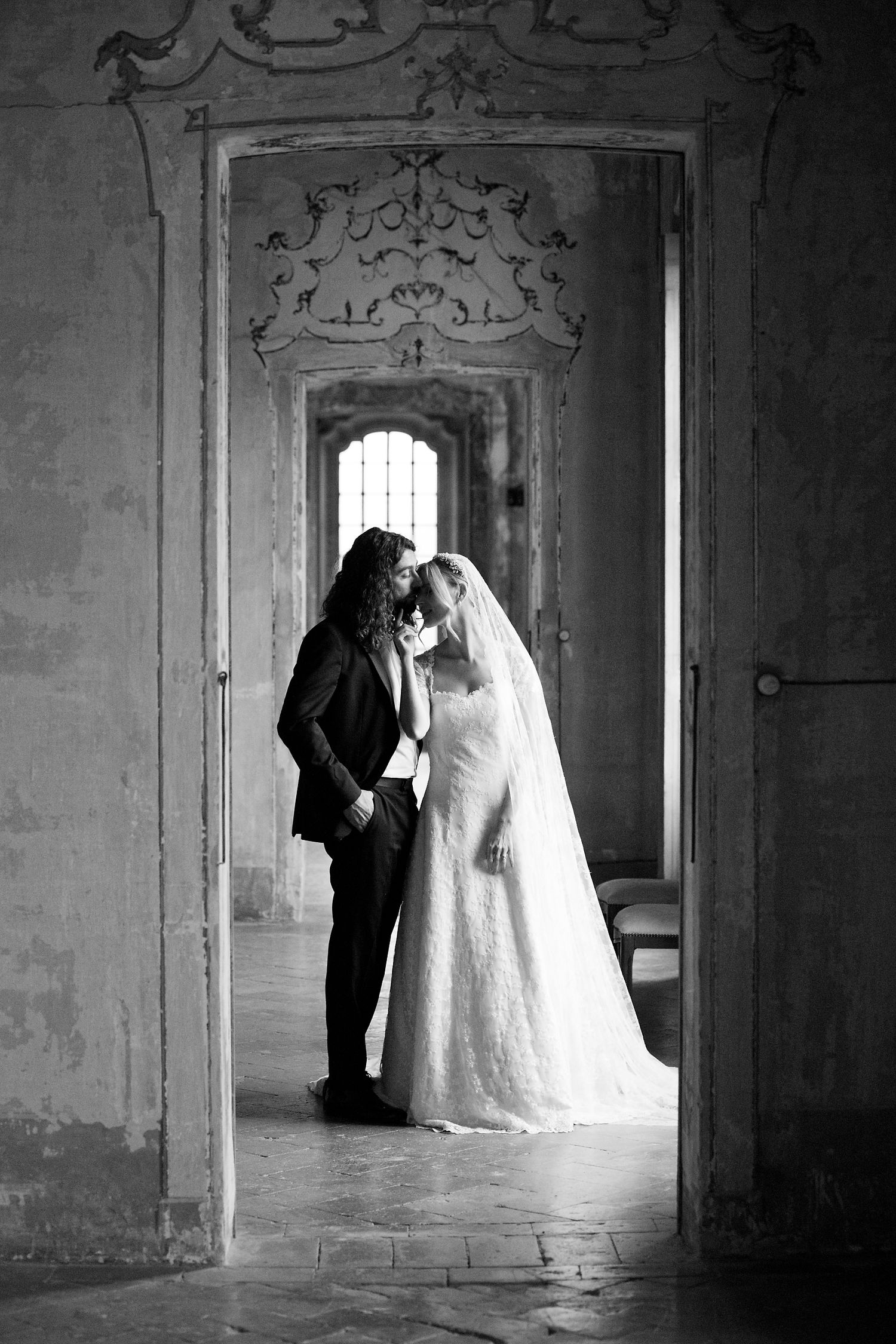 A black and white wedding portrait showing a tender moment between newlyweds in a historic palace doorway.