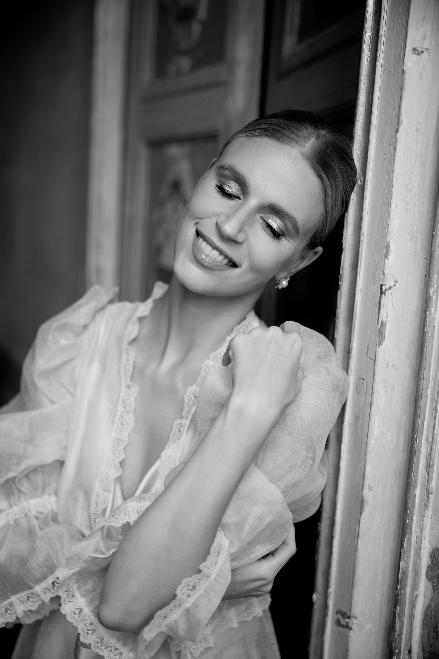 Black and white portrait in feminine lace robe showing joyful expression by vintage doorway.