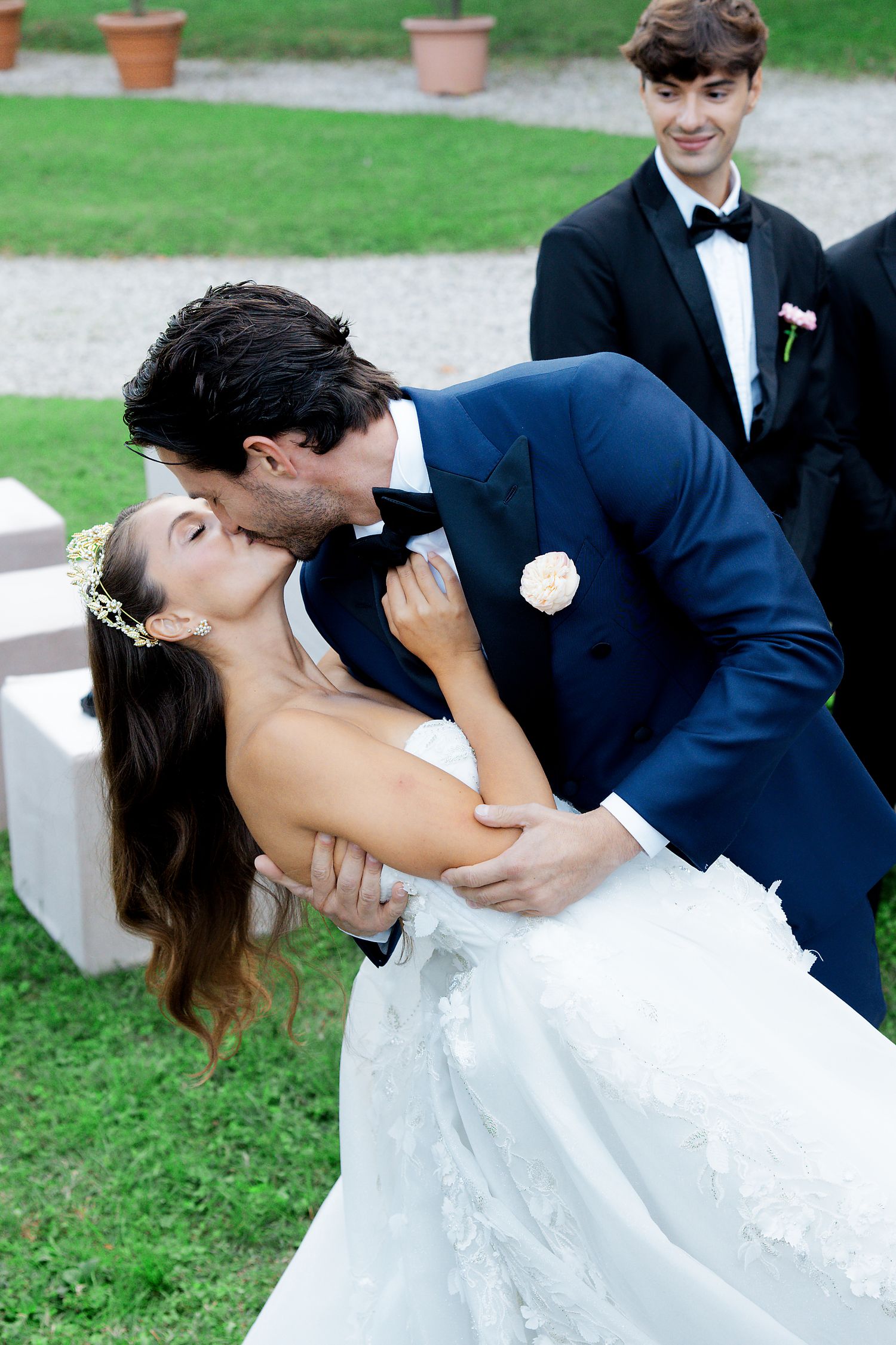 A romantic dip kiss between newlyweds on manicured garden grounds.
