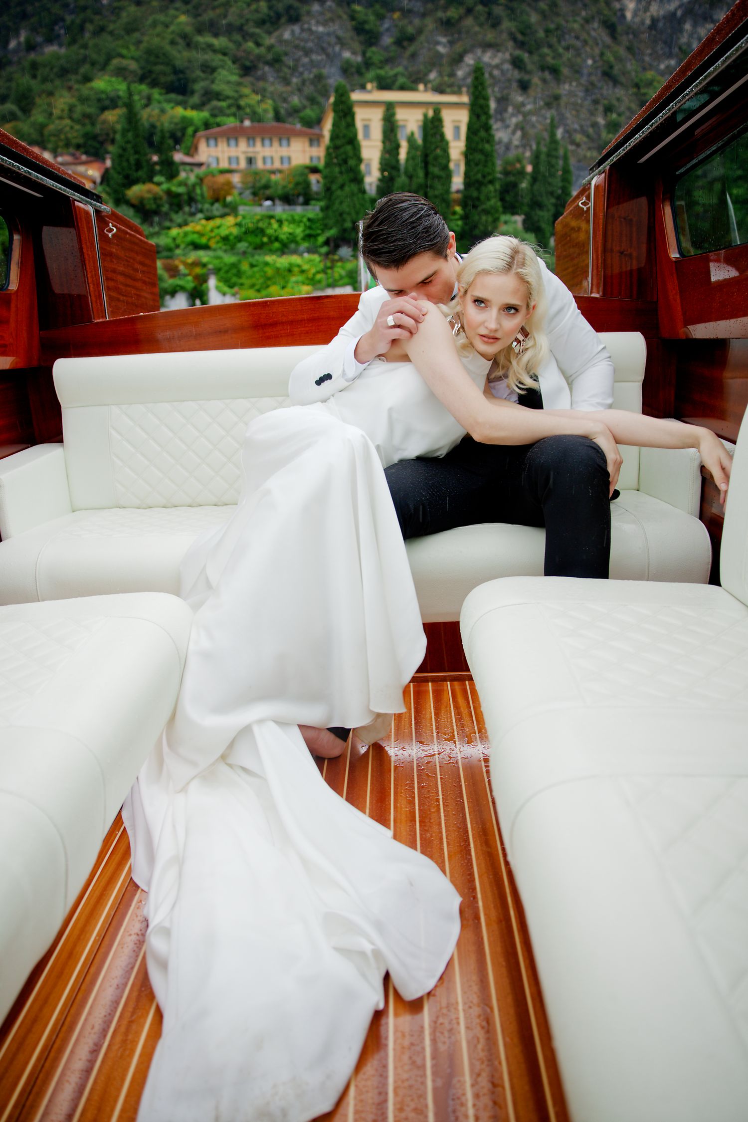 Wedding couple relaxing on luxurious white leather seats of vintage wooden boat.