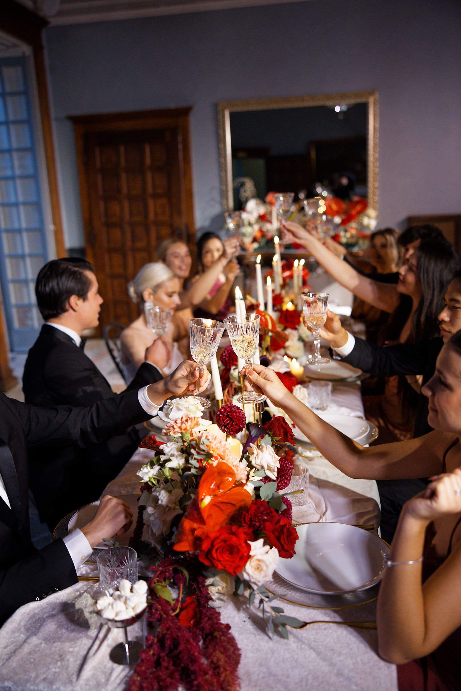 Wedding reception table with vibrant floral centerpieces and guests raising glasses in a toast celebration.