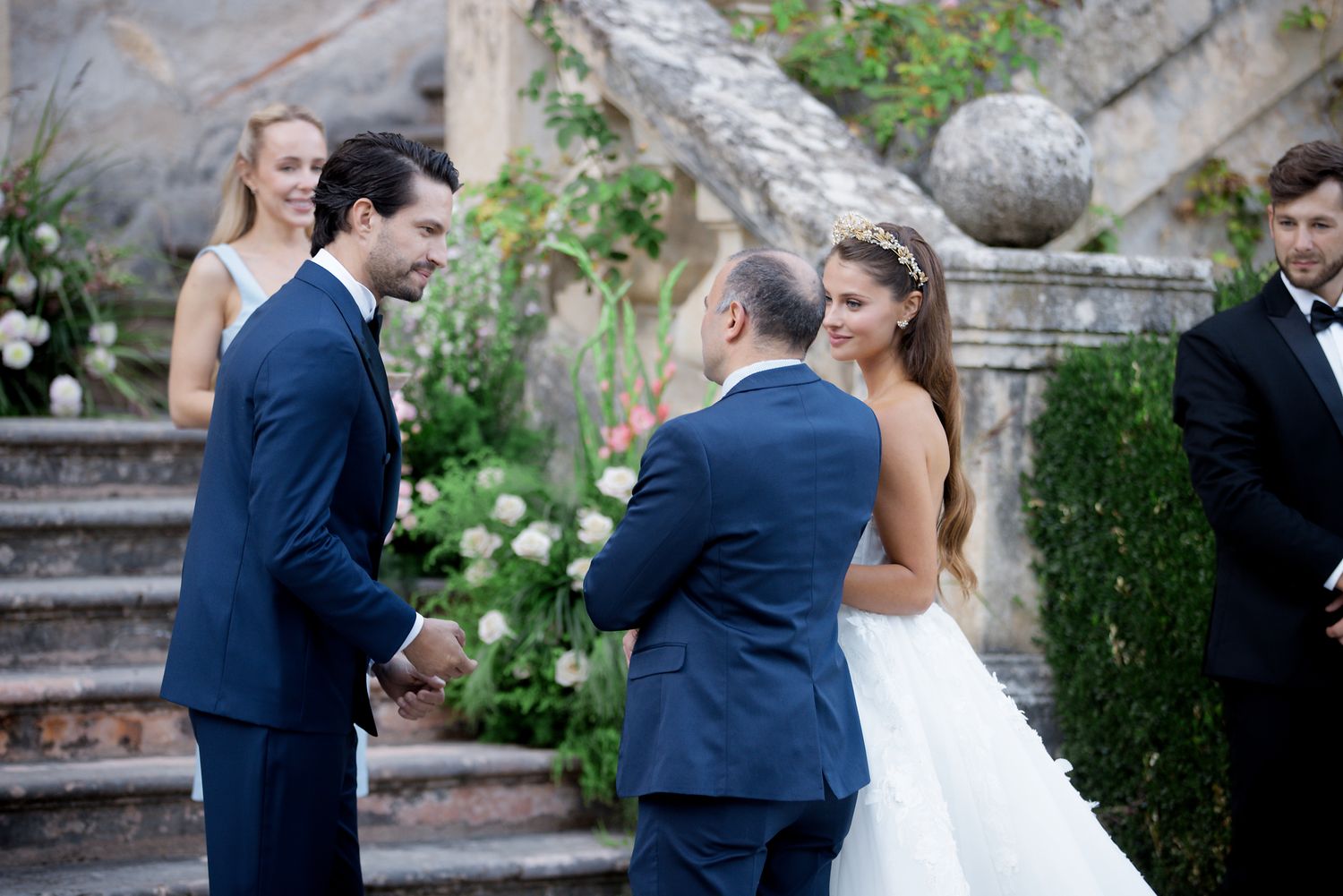 People in formal attire gather on stone steps during an elegant outdoor wedding ceremony.