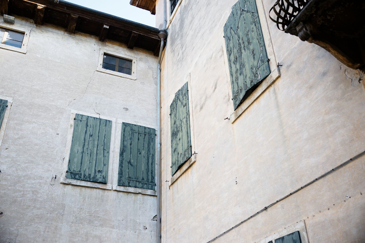 White Mediterranean building facade with traditional green wooden shutters on windows viewed from a low angle.