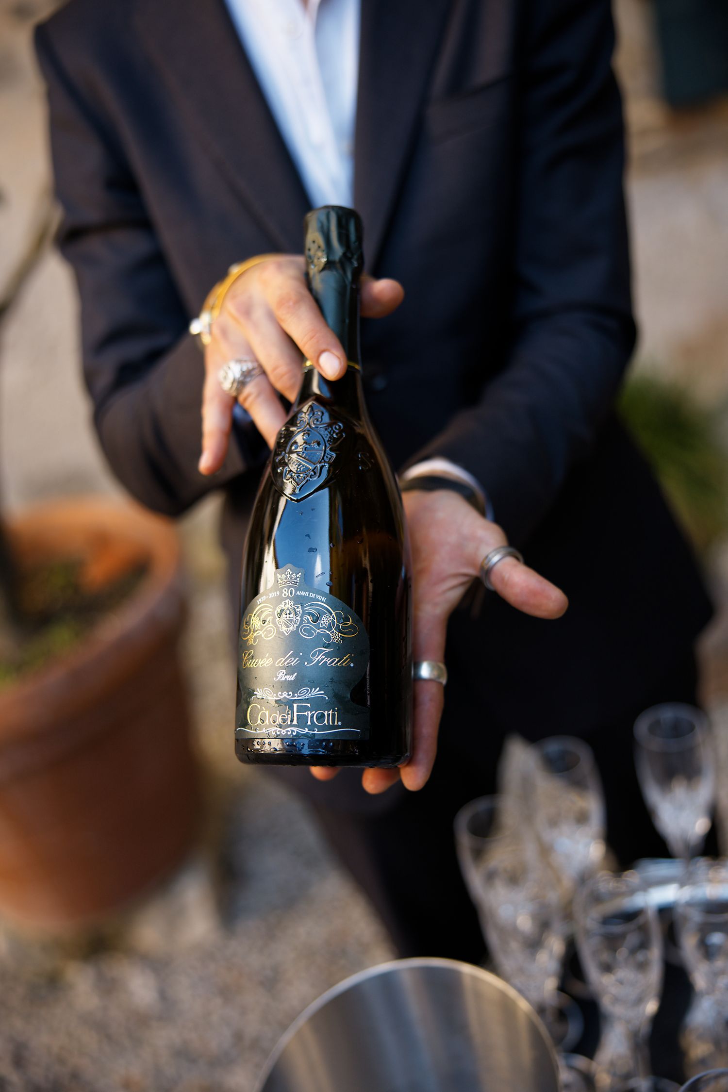 Hands holding an ornate blue wine bottle at an elegant event with champagne glasses in the background.