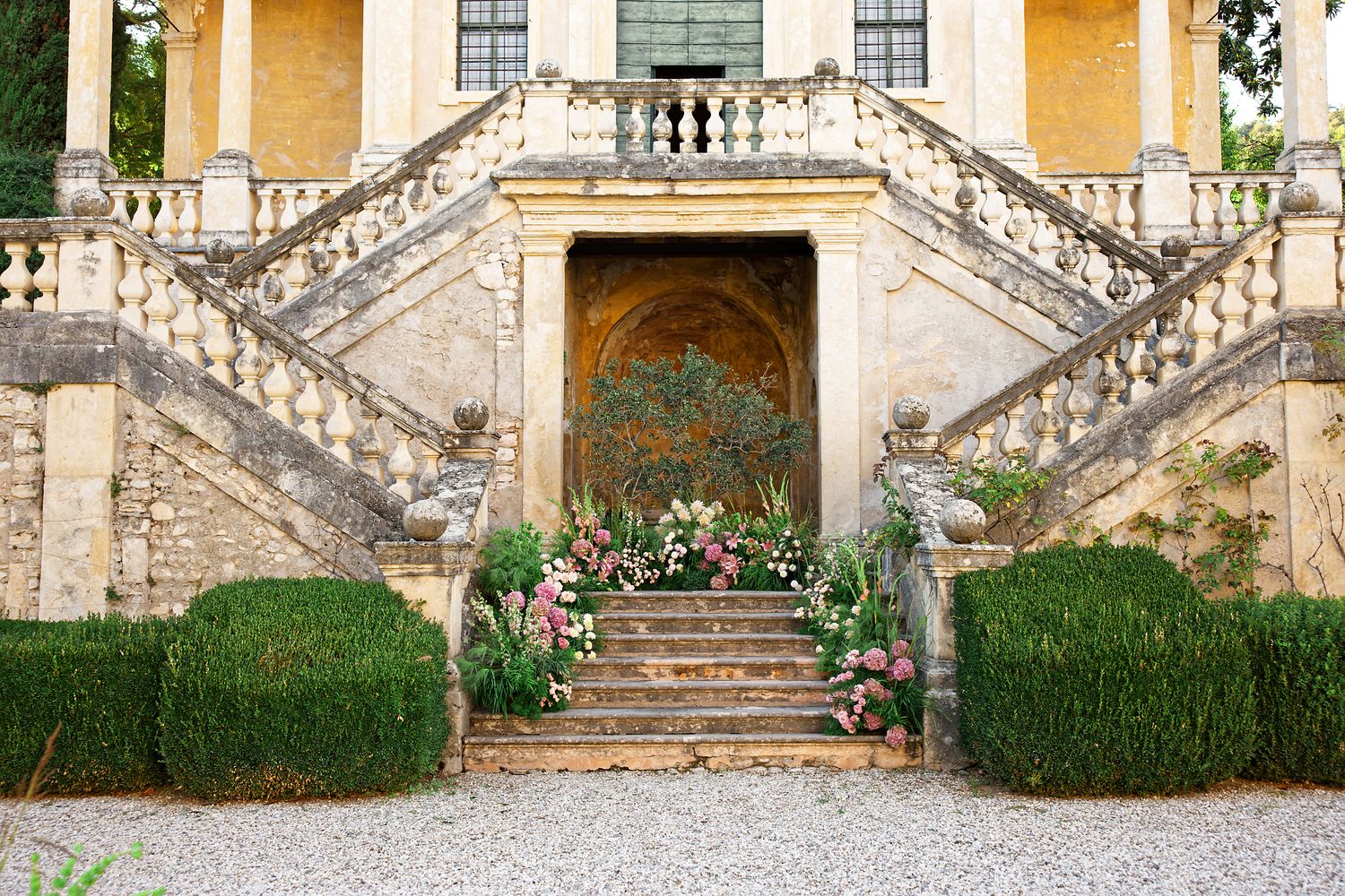 Elegant villa entrance with symmetrical stone staircase decorated with floral arrangements.