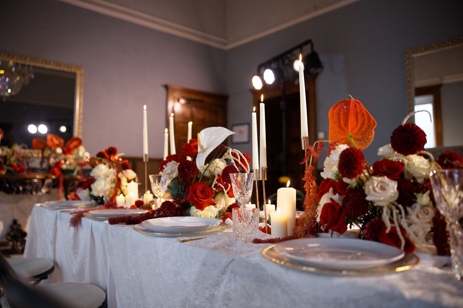Romantic table setting with red floral arrangements and glowing candles for wedding reception.