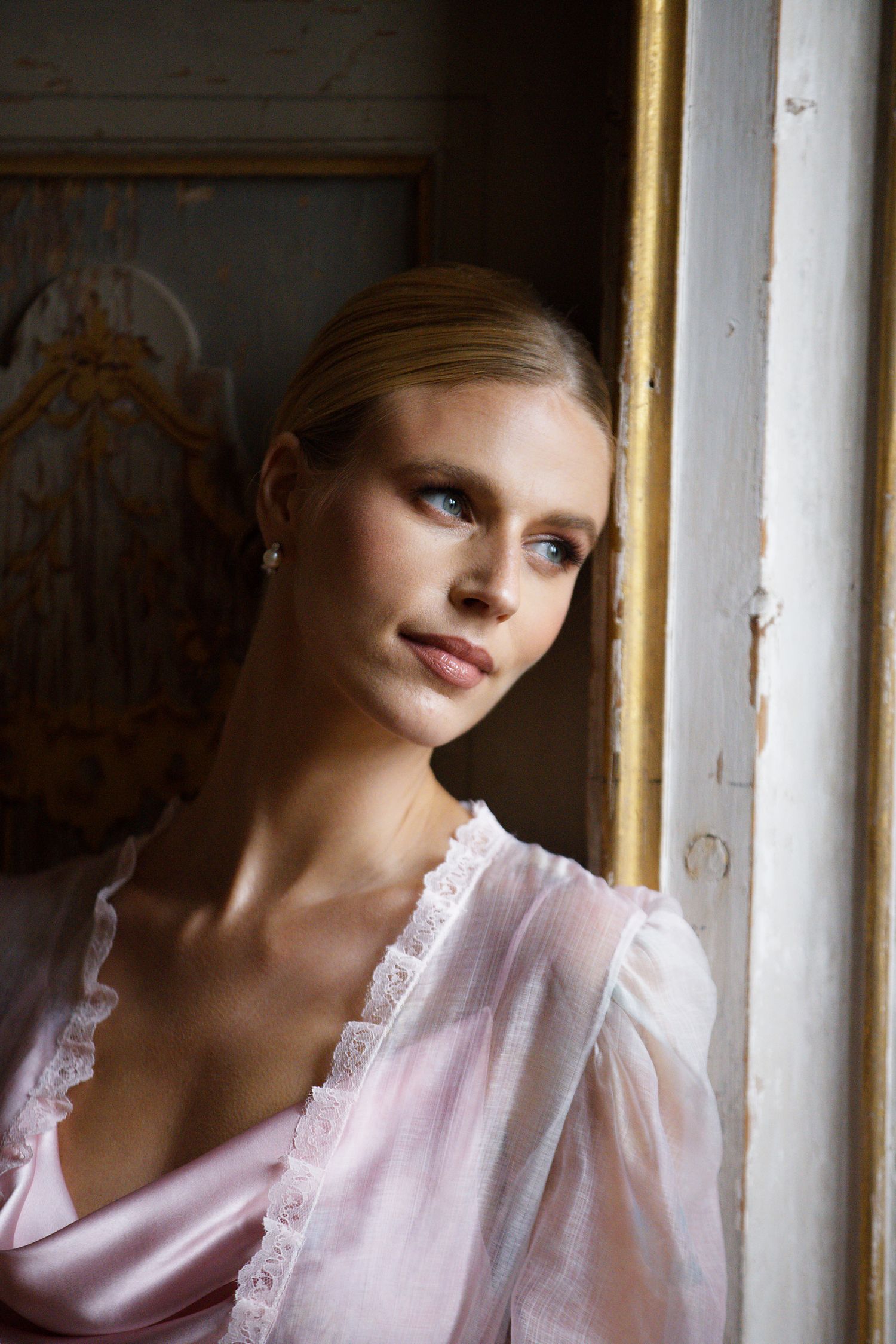 Soft natural light portrait by window in vintage-style pink silk ensemble.