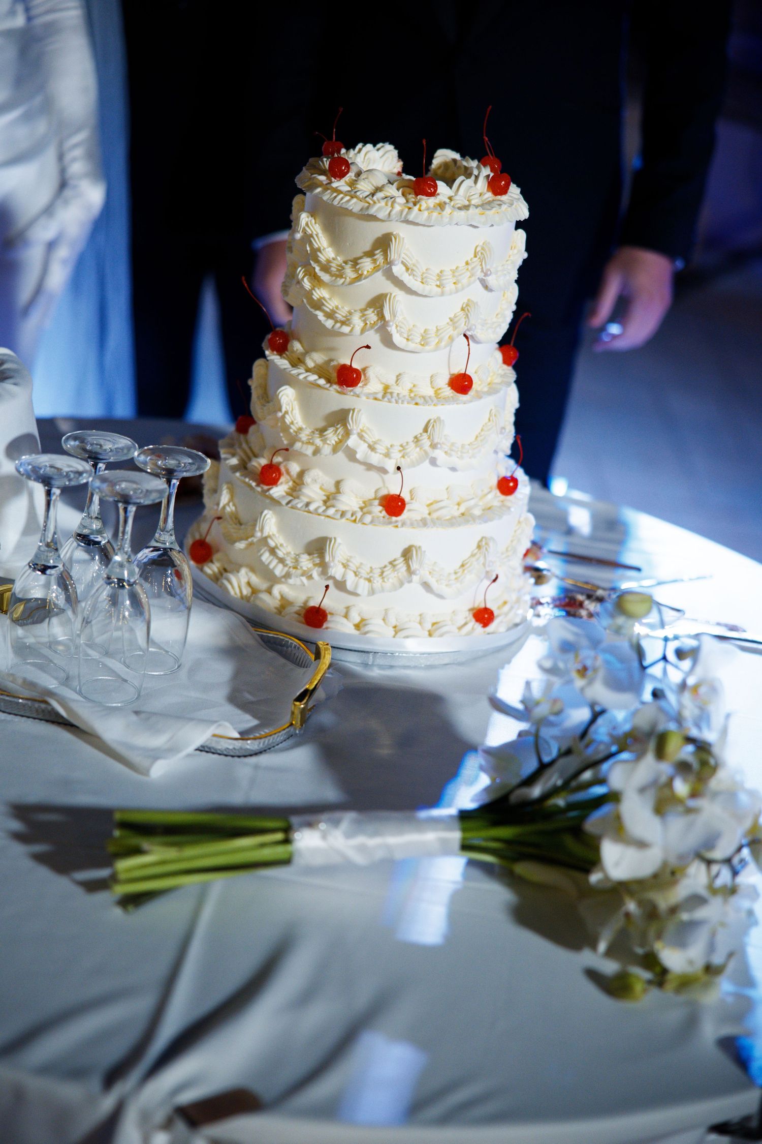 An elegant white wedding cake with delicate frosting details and red accents surrounded by champagne glasses.