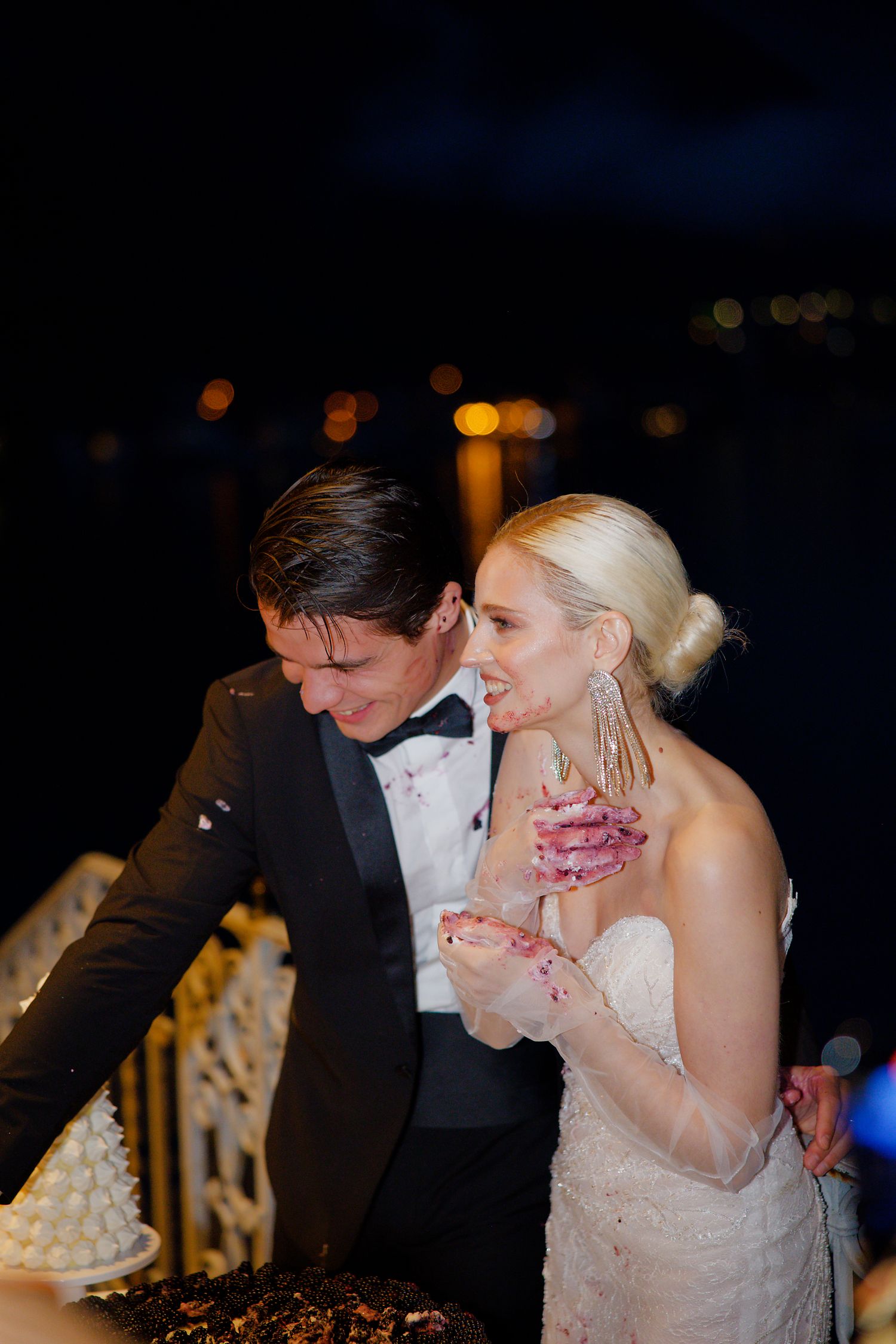 A joyful celebration moment at night with formal attire and glowing lights in the background.