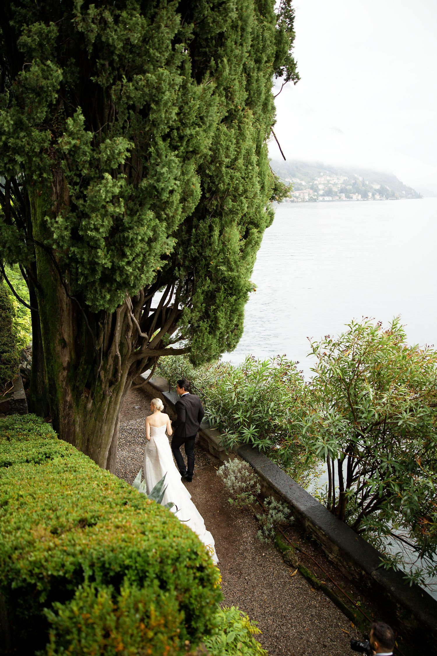 Garden pathway along a lakeside with tall cypress trees and water views.