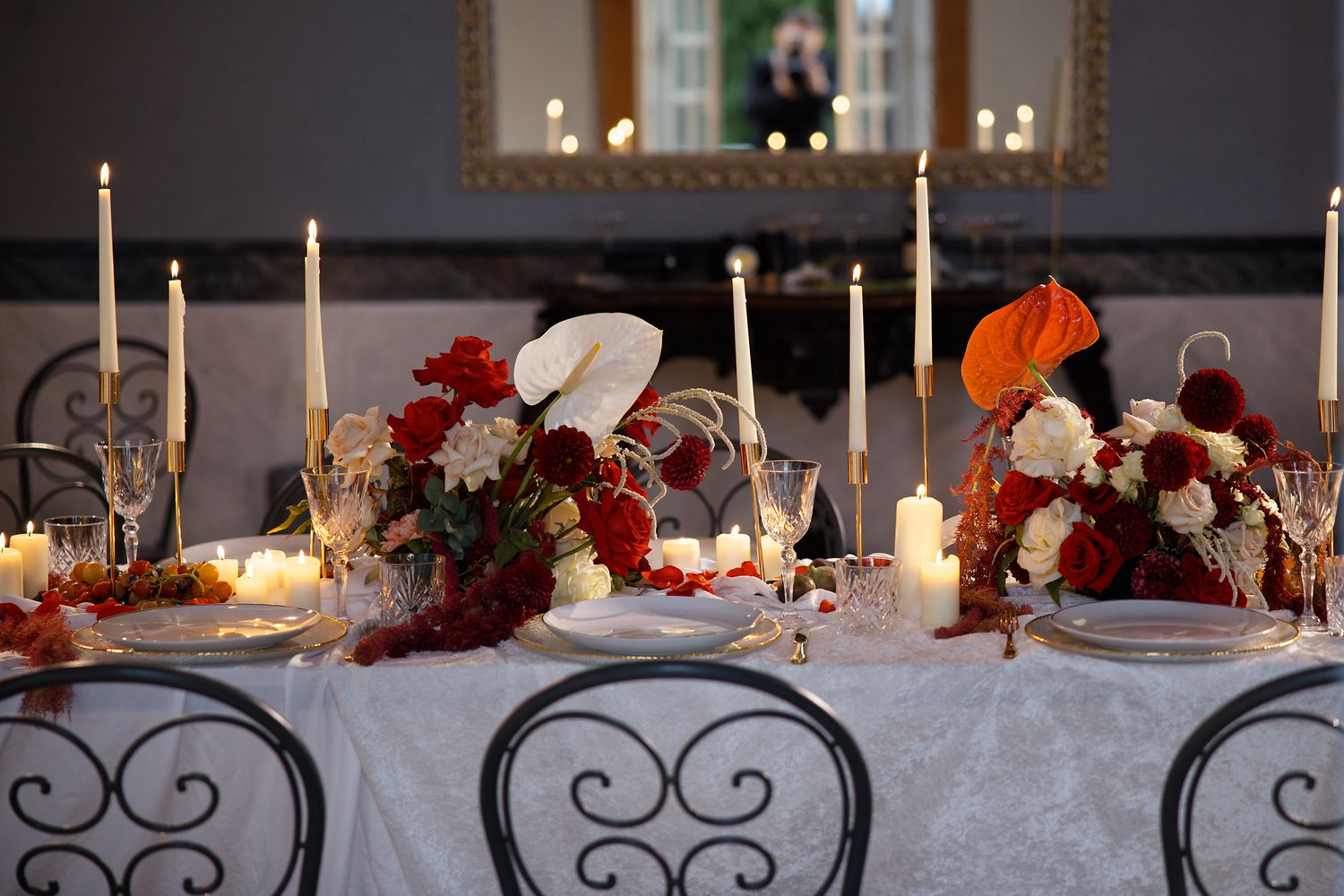 Romantic wedding table setting with red floral centerpieces and glowing candles.