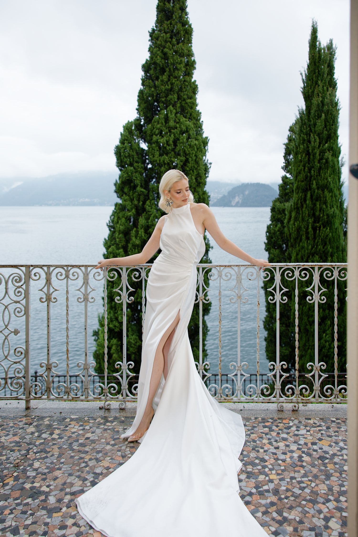 Elegant white dress with flowing train photographed against Lake Como backdrop with cypress trees.