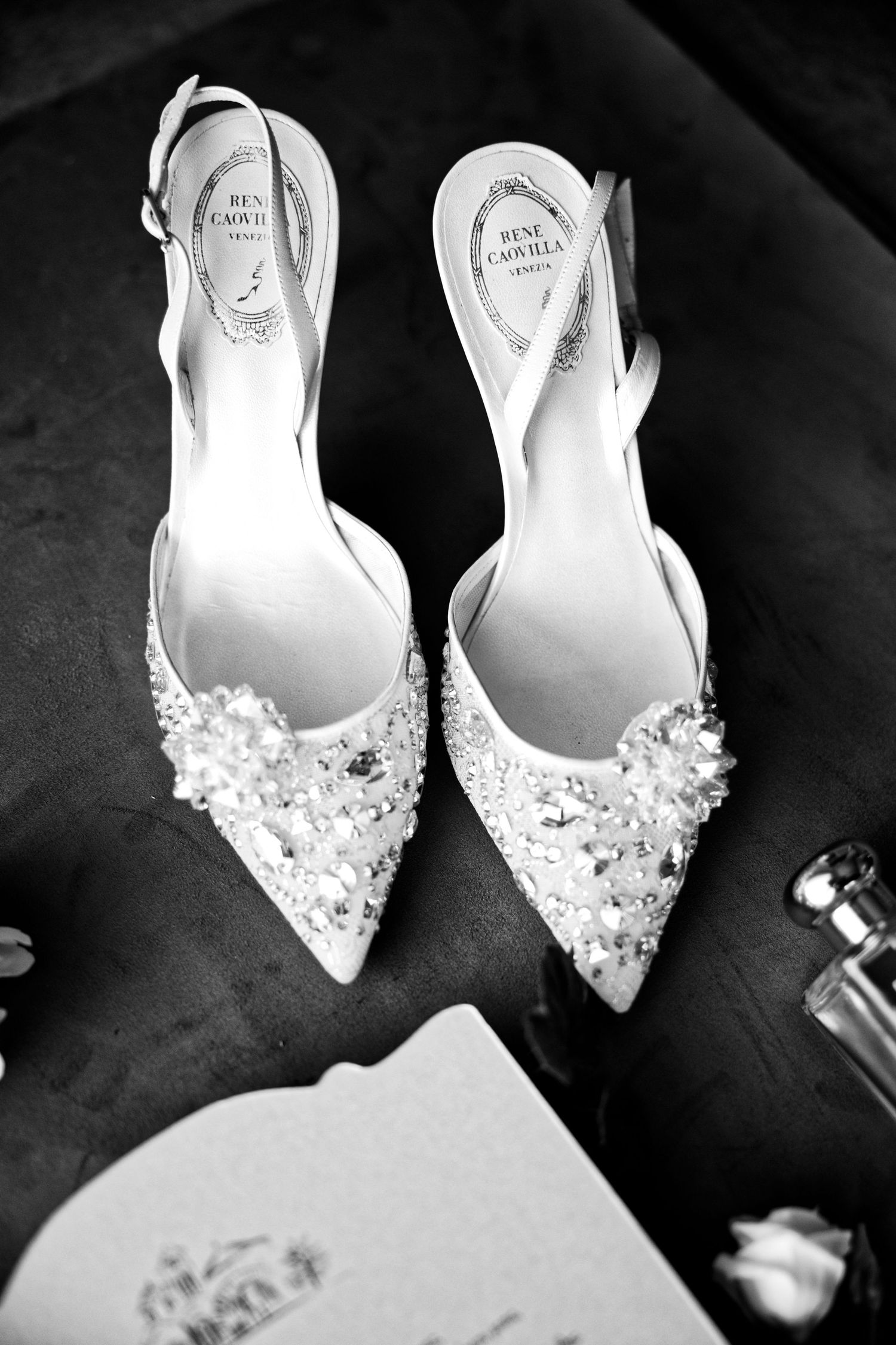 Elegant white bridal shoes with delicate floral embellishments and pearls photographed in black and white.