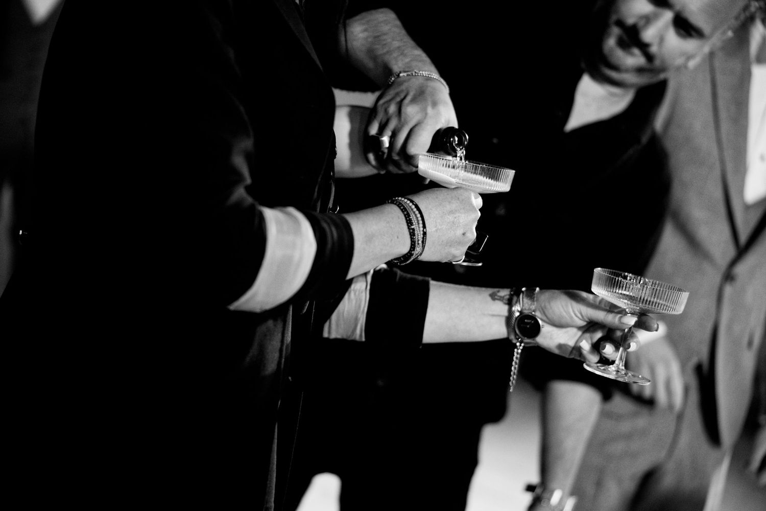 Black and white photo of hands pouring champagne into glasses at formal event.