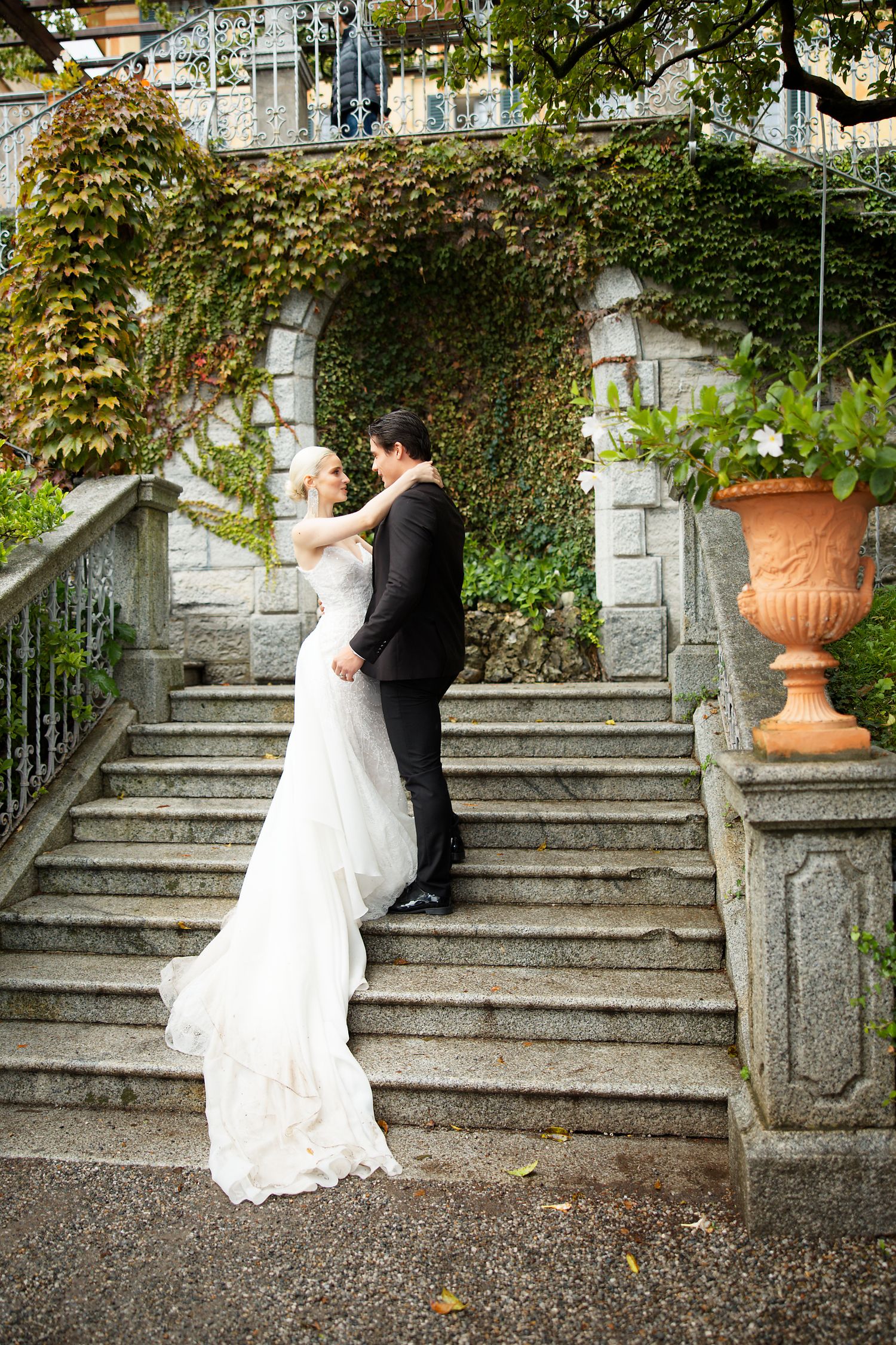 Romantic wedding photo on stone steps with ivy-covered walls and classical architecture.