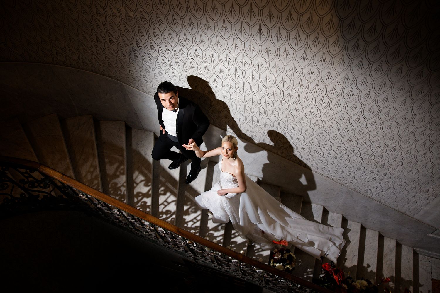 Dramatic silhouette of couple on ornate staircase with patterned wall backdrop.