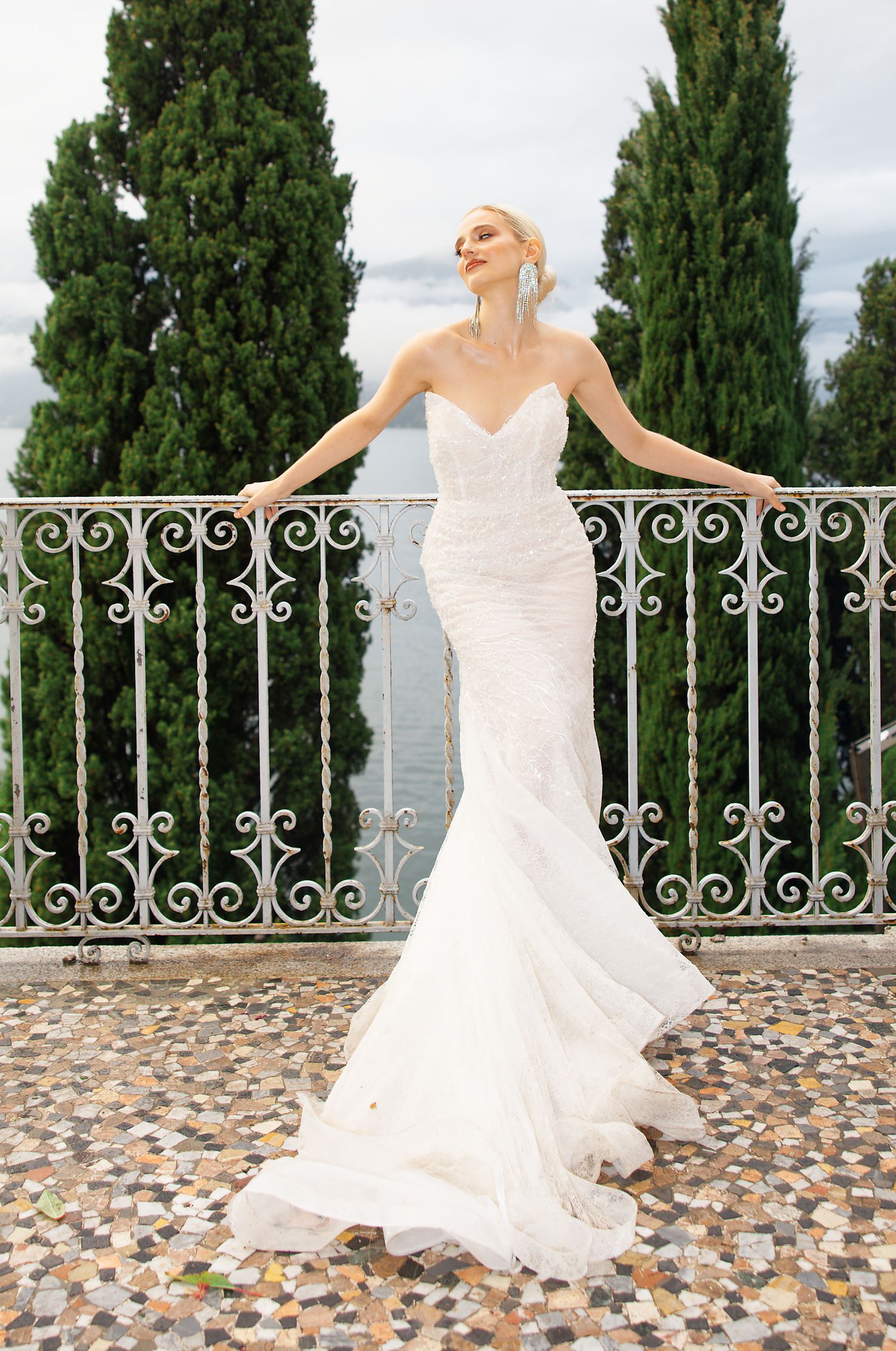 Fitted mermaid wedding gown showcased on stone terrace with cypress trees in background.