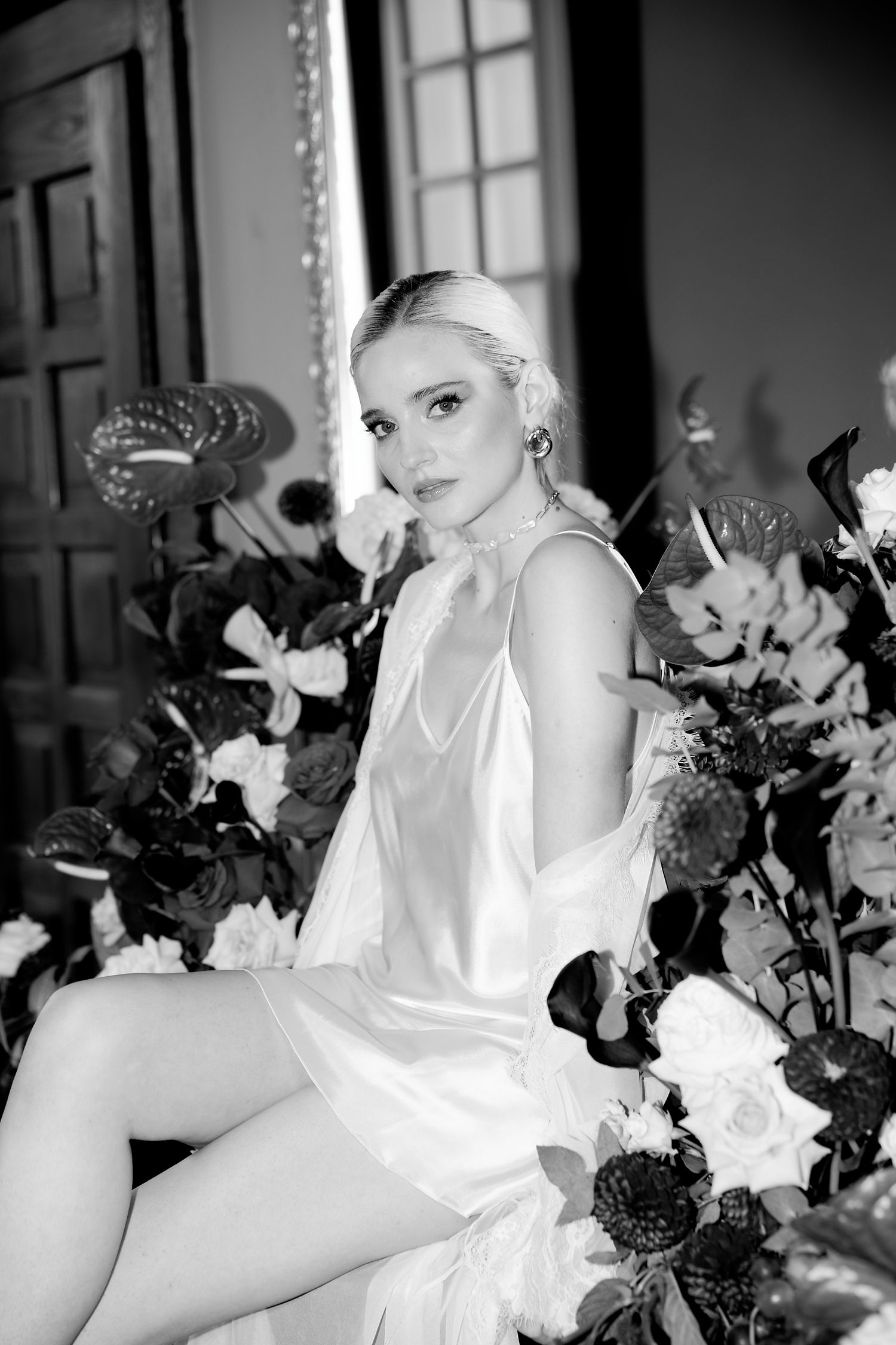 Elegant black and white bridal portrait with roses and floral arrangements in an ornate indoor setting.