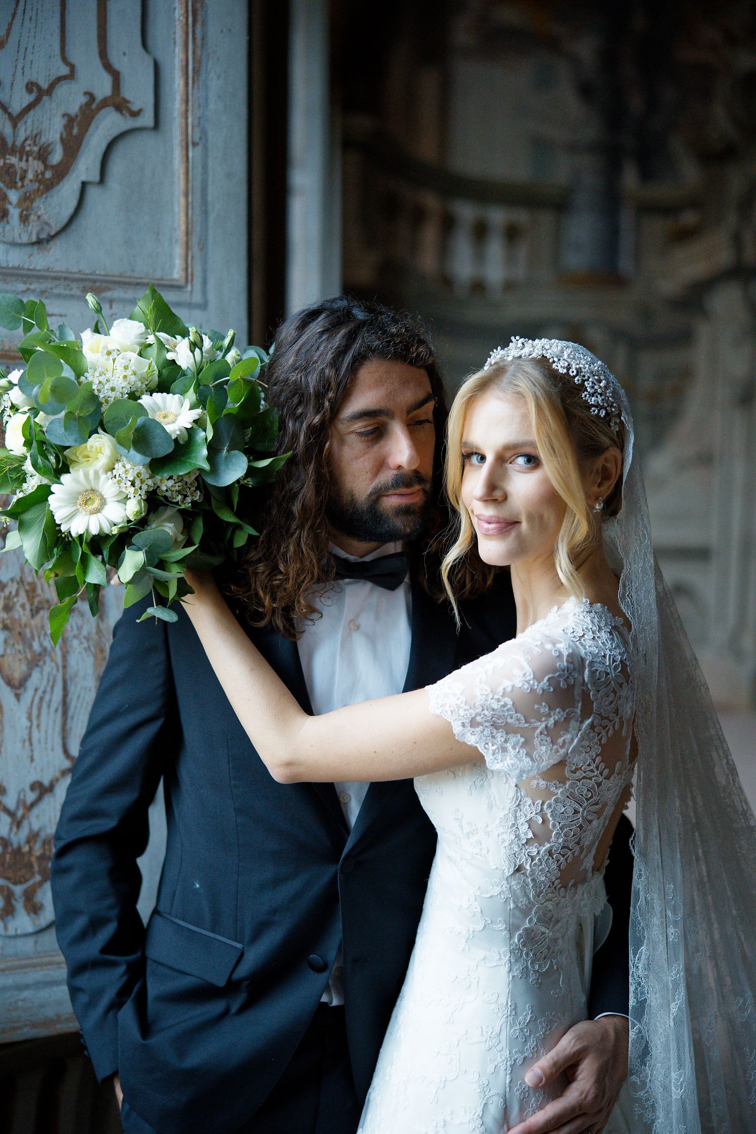 A romantic wedding portrait with white floral arrangements and lace details in an elegant vintage setting.