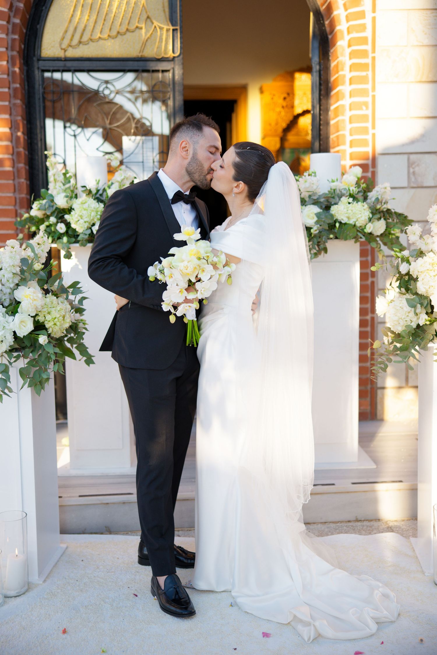 A romantic wedding moment under a floral arch with white hydrangeas and greenery decorations.