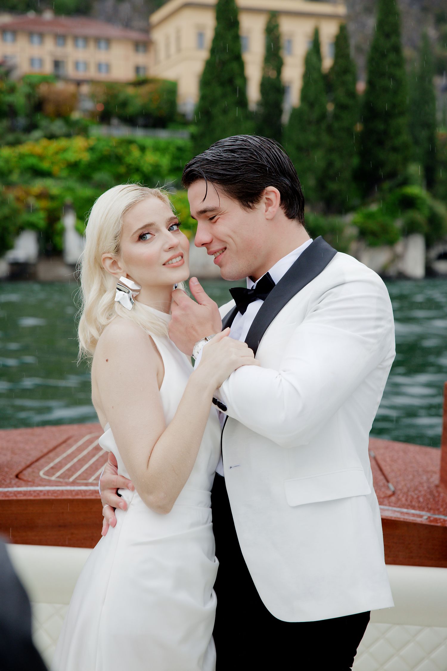 Wedding couple sharing romantic moment on vintage wooden boat with Italian lakeside scenery.