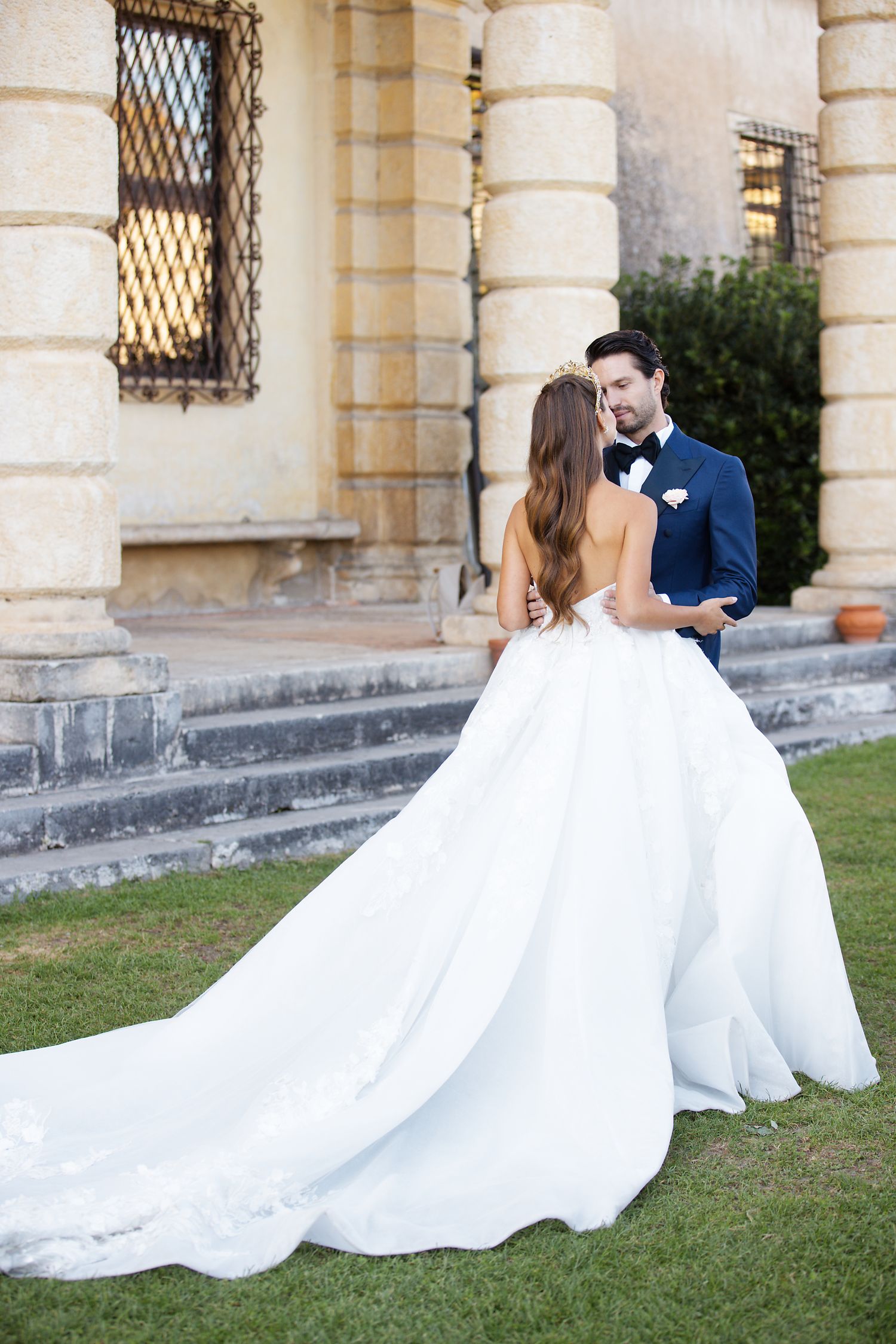 Wedding couple embraces on stone steps of elegant Mediterranean villa during sunset photo session.
