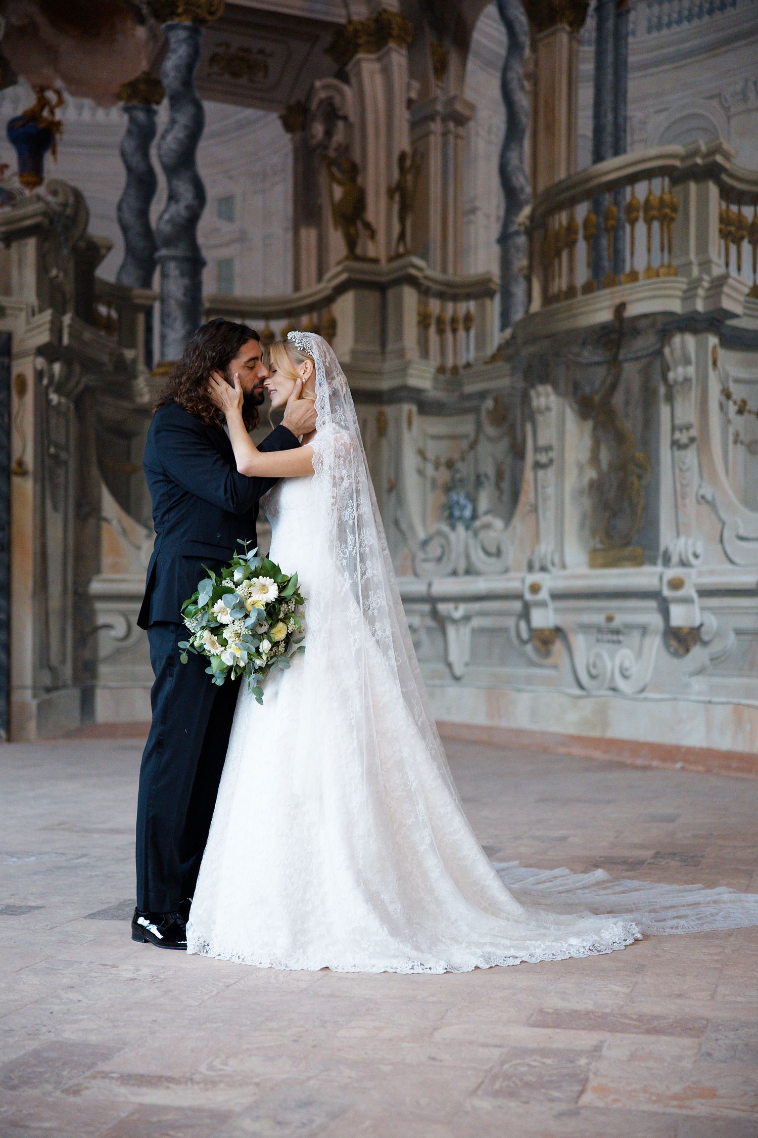 Wedding couple shares an intimate moment in a historic palace setting with ornate architectural details.