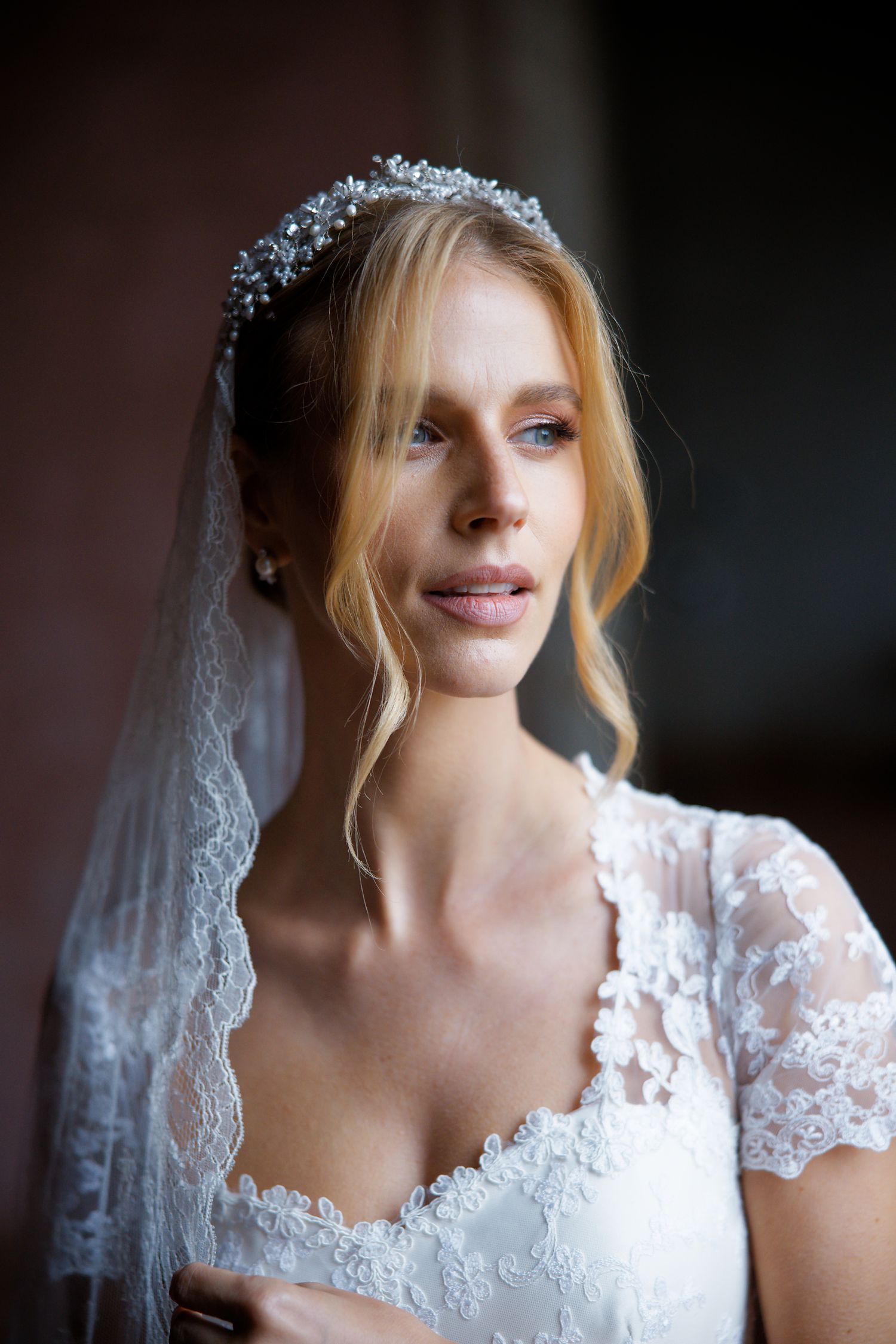 A bride wearing a delicate lace wedding dress with short sleeves and crystal headpiece with flowing veil.