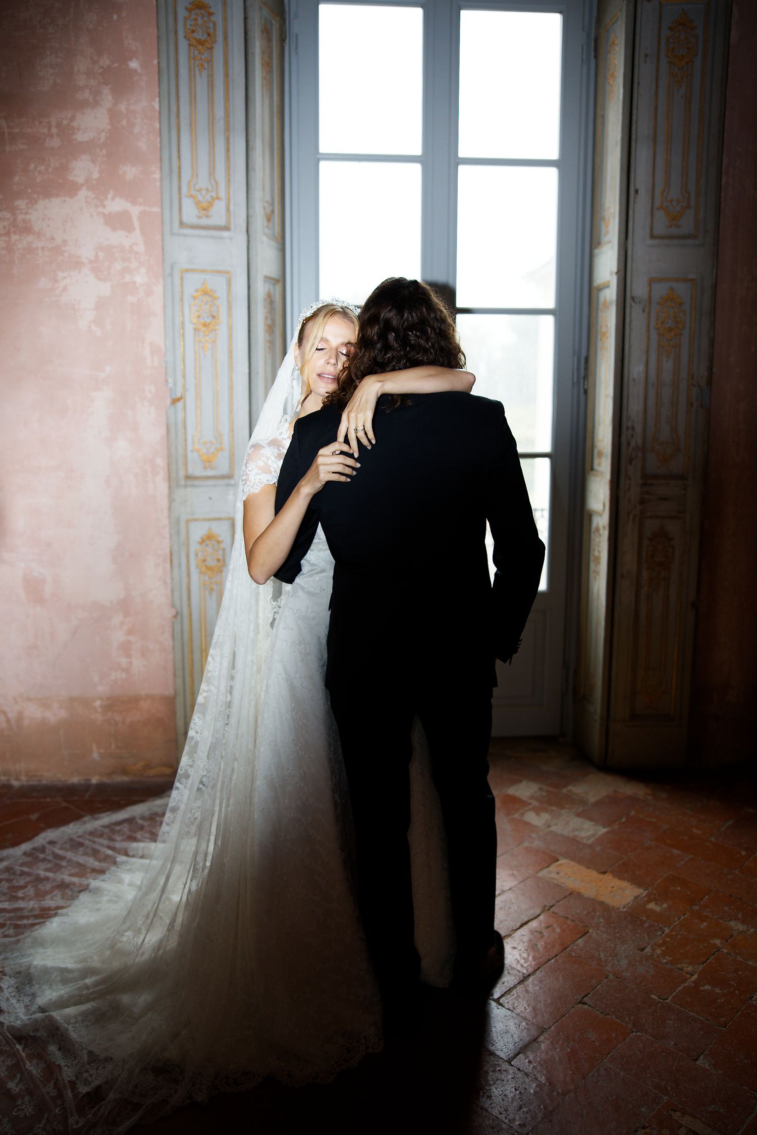 A tender embrace between newlyweds in a sunlit historic room with pink walls.