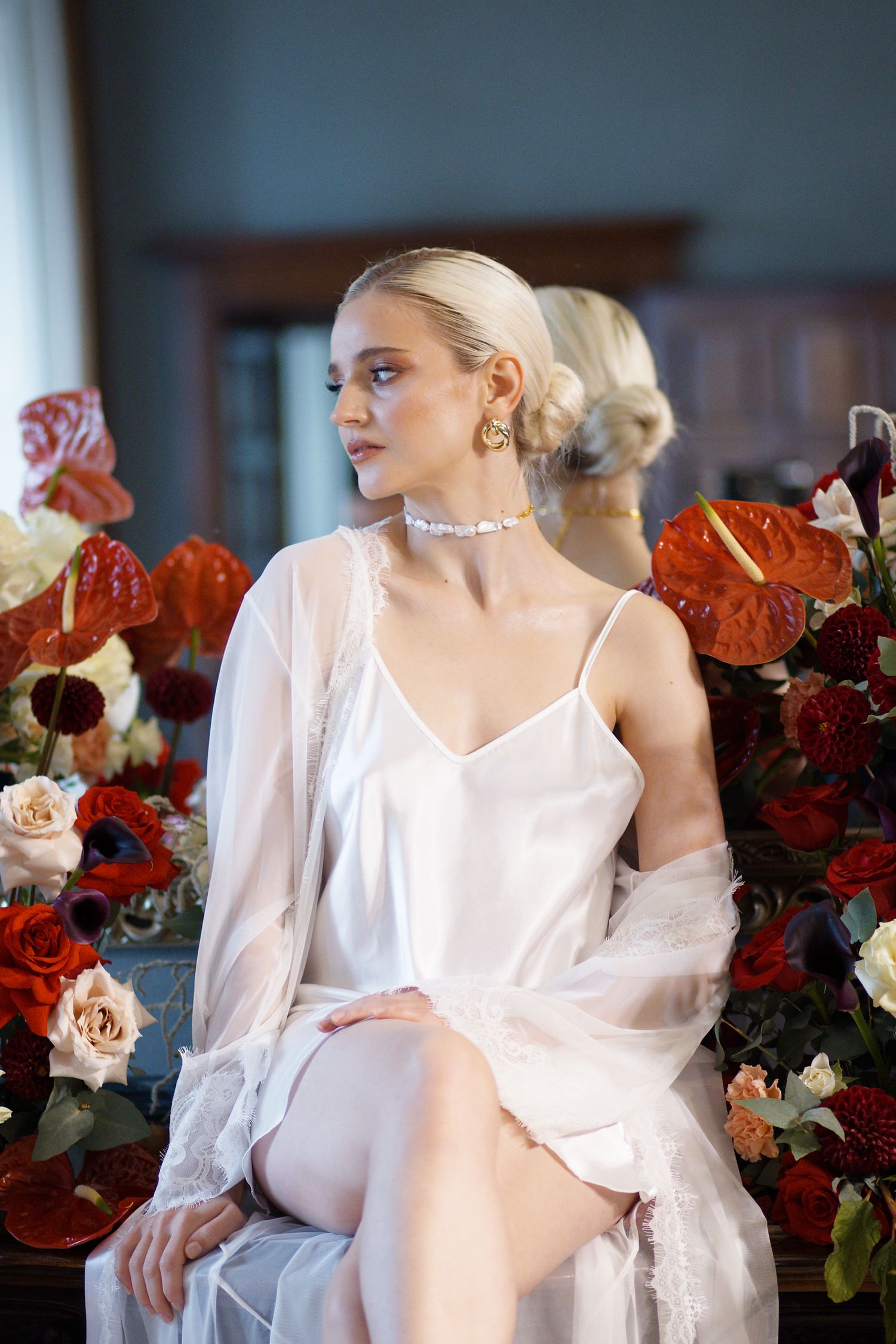 Romantic boudoir setting with soft white silk lingerie surrounded by deep red and blush floral arrangements.