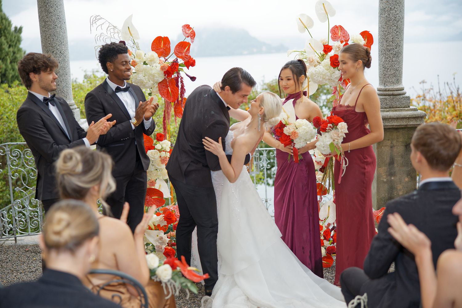 Wedding ceremony moment with bridal party celebrating under floral arch overlooking lake.