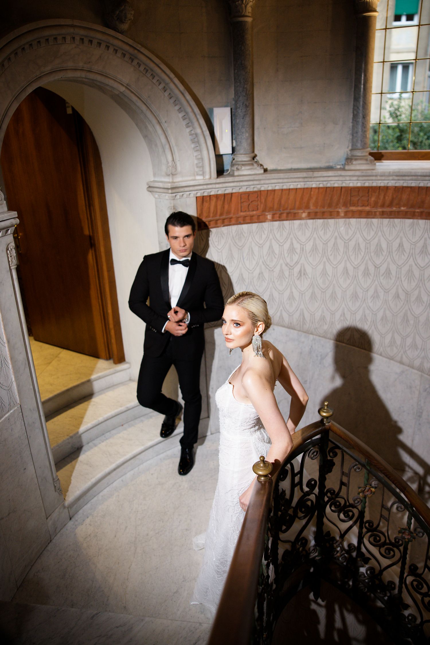 A dramatic staircase wedding photo featuring elegant formal attire and architectural details.