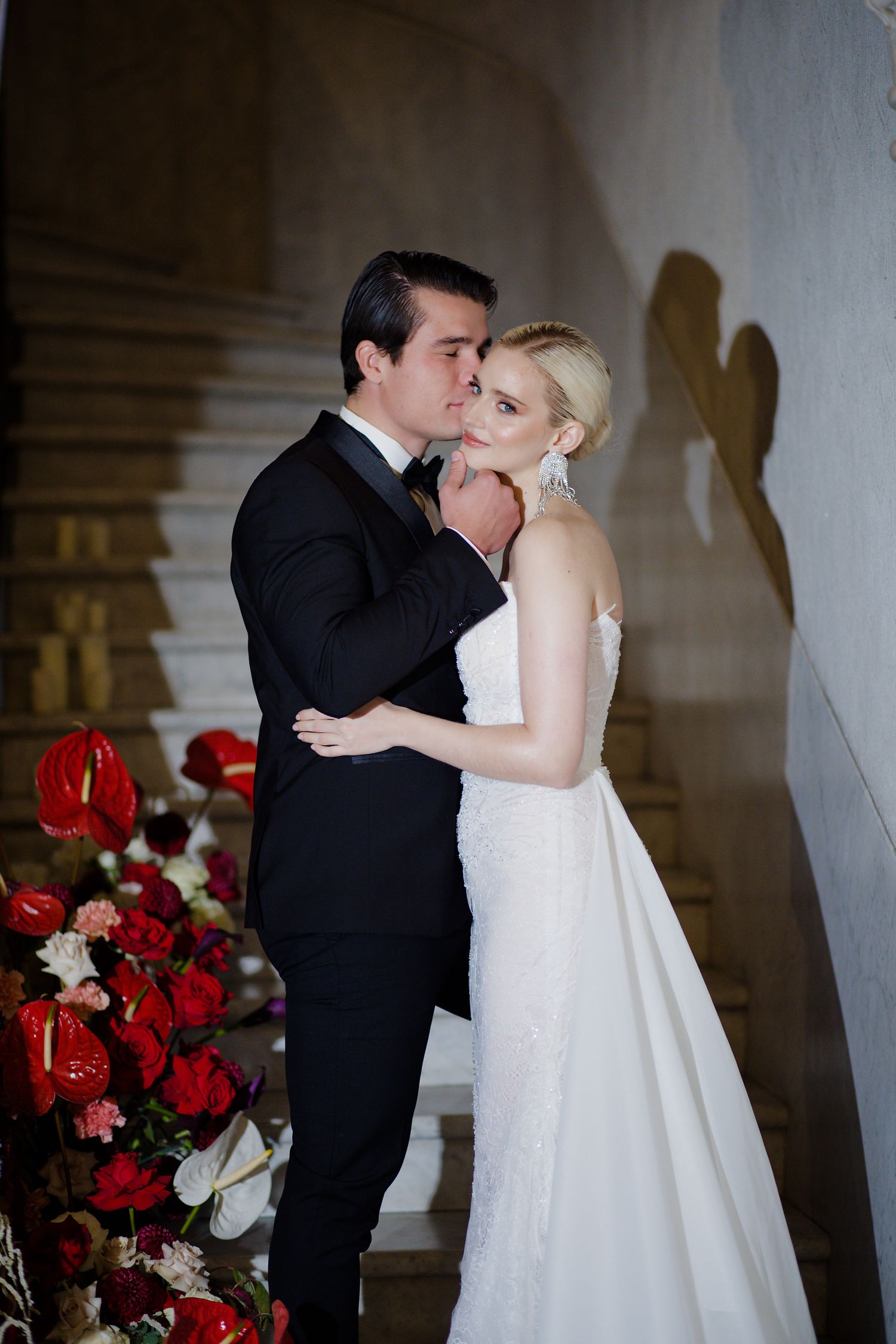 Romantic wedding portrait with couple embracing near red floral decorations.